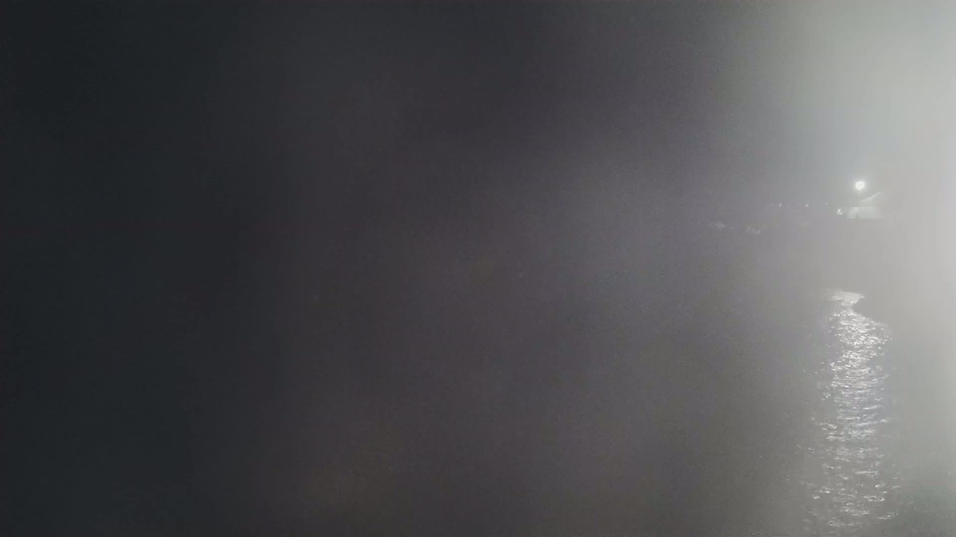 A dimly lit body of water is shrouded in thick fog at night, with a single light source visible in the distance.