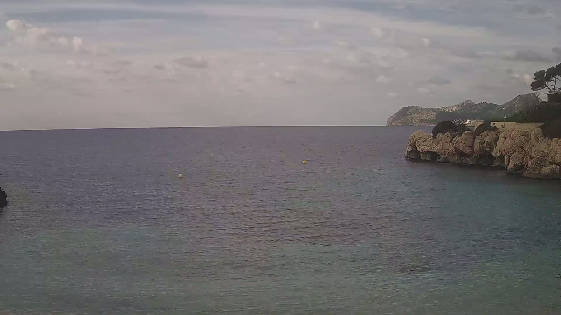 A calm sea stretches to a distant, mountainous coastline under a partly cloudy sky.