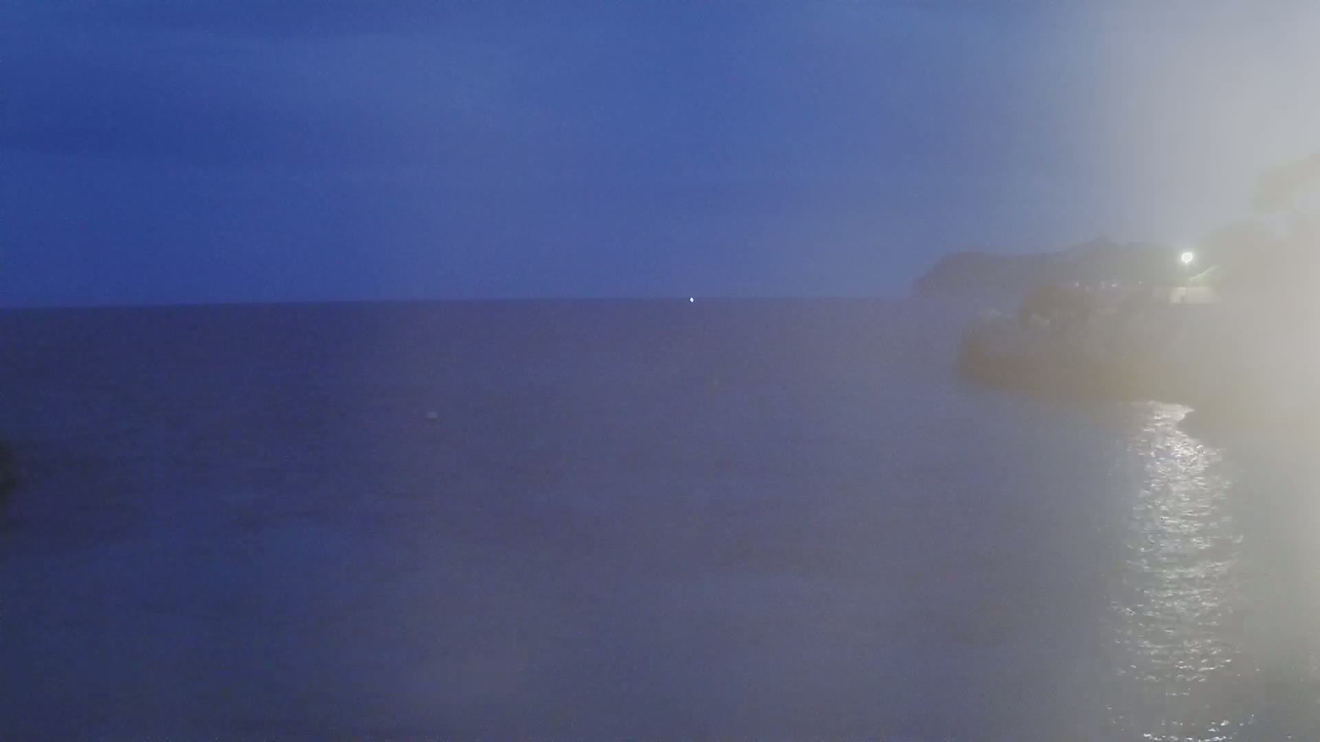 A hazy, dark blue ocean meets a similarly hazy, dark shoreline under a twilight sky.