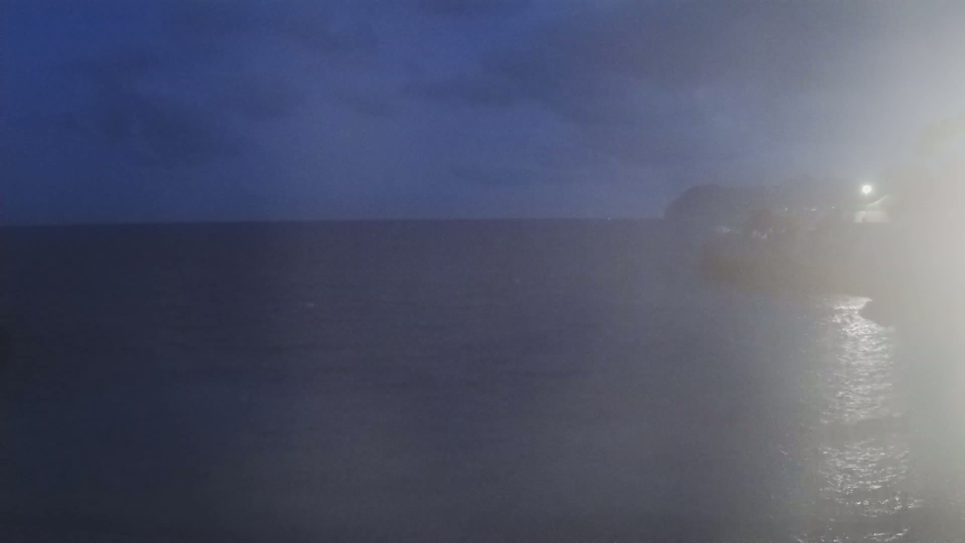A hazy, dark-blue ocean is visible under a dusky sky, with a dimly lit landmass in the background.