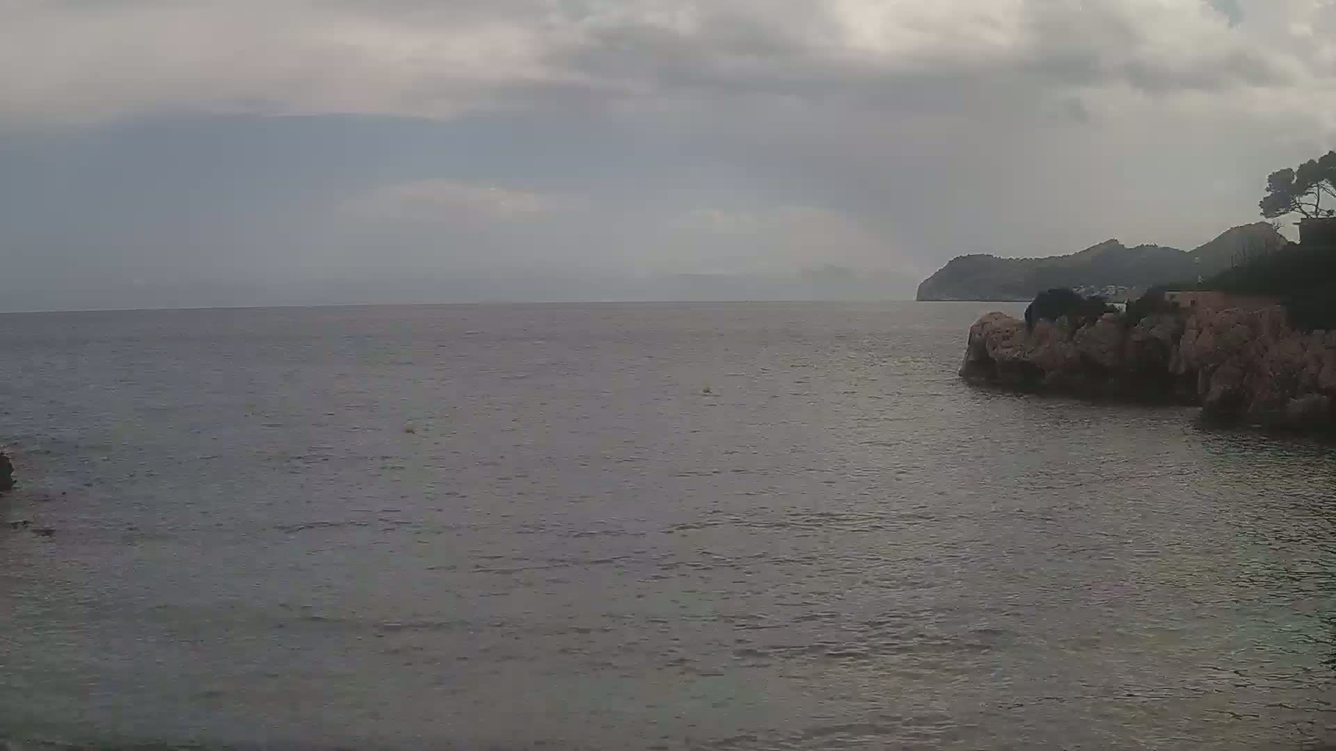 A calm, gray sea meets a rocky shore under an overcast sky.