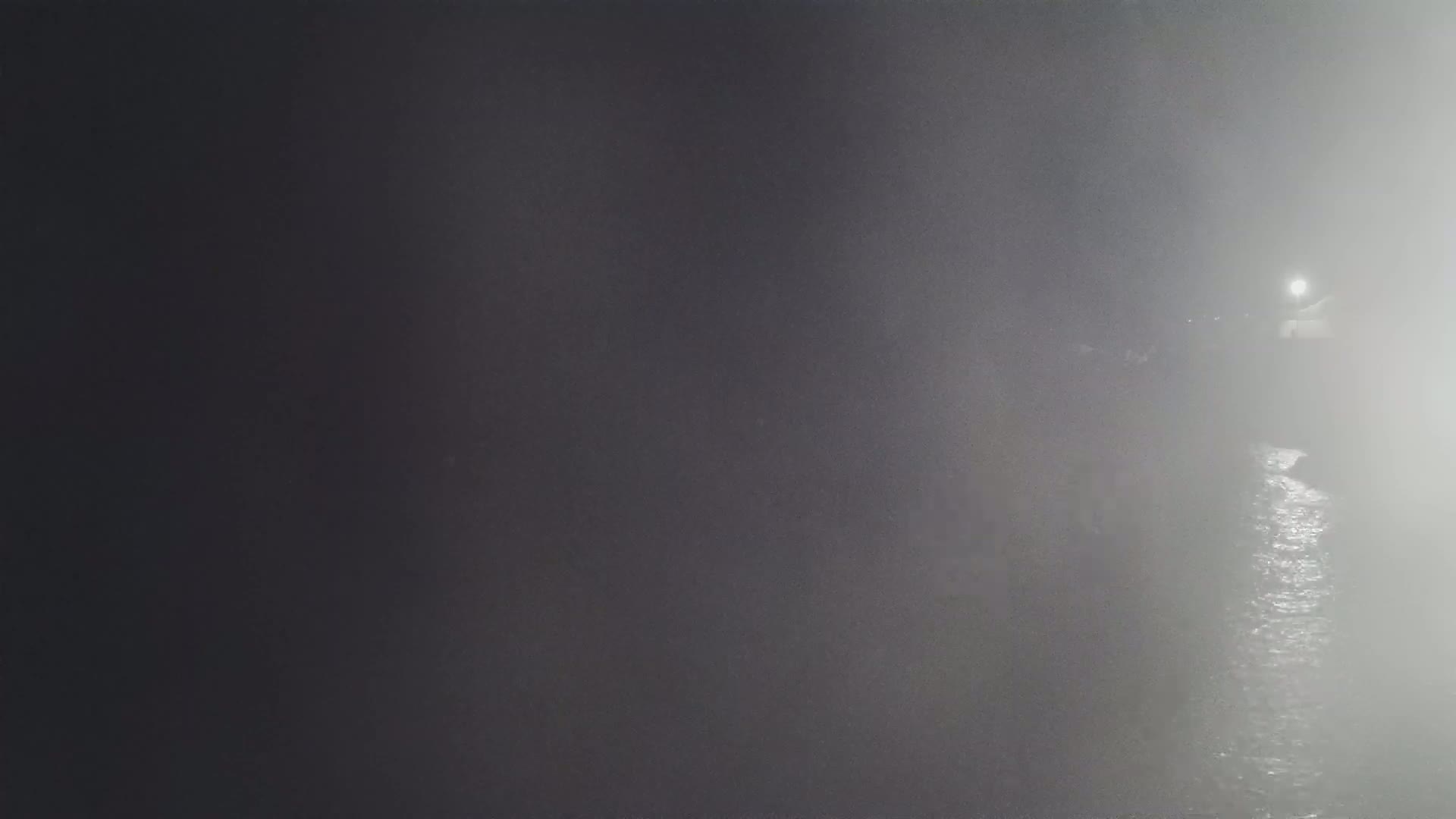 A dimly lit body of water is shrouded in heavy fog at night.