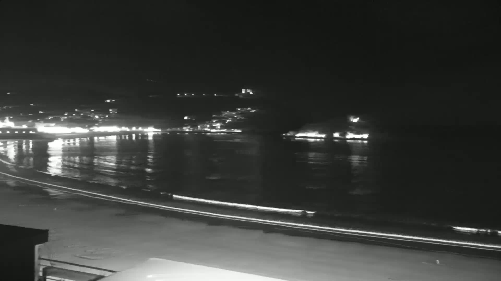 A nighttime view of a calm body of water reflecting the lights of a town on the shore.