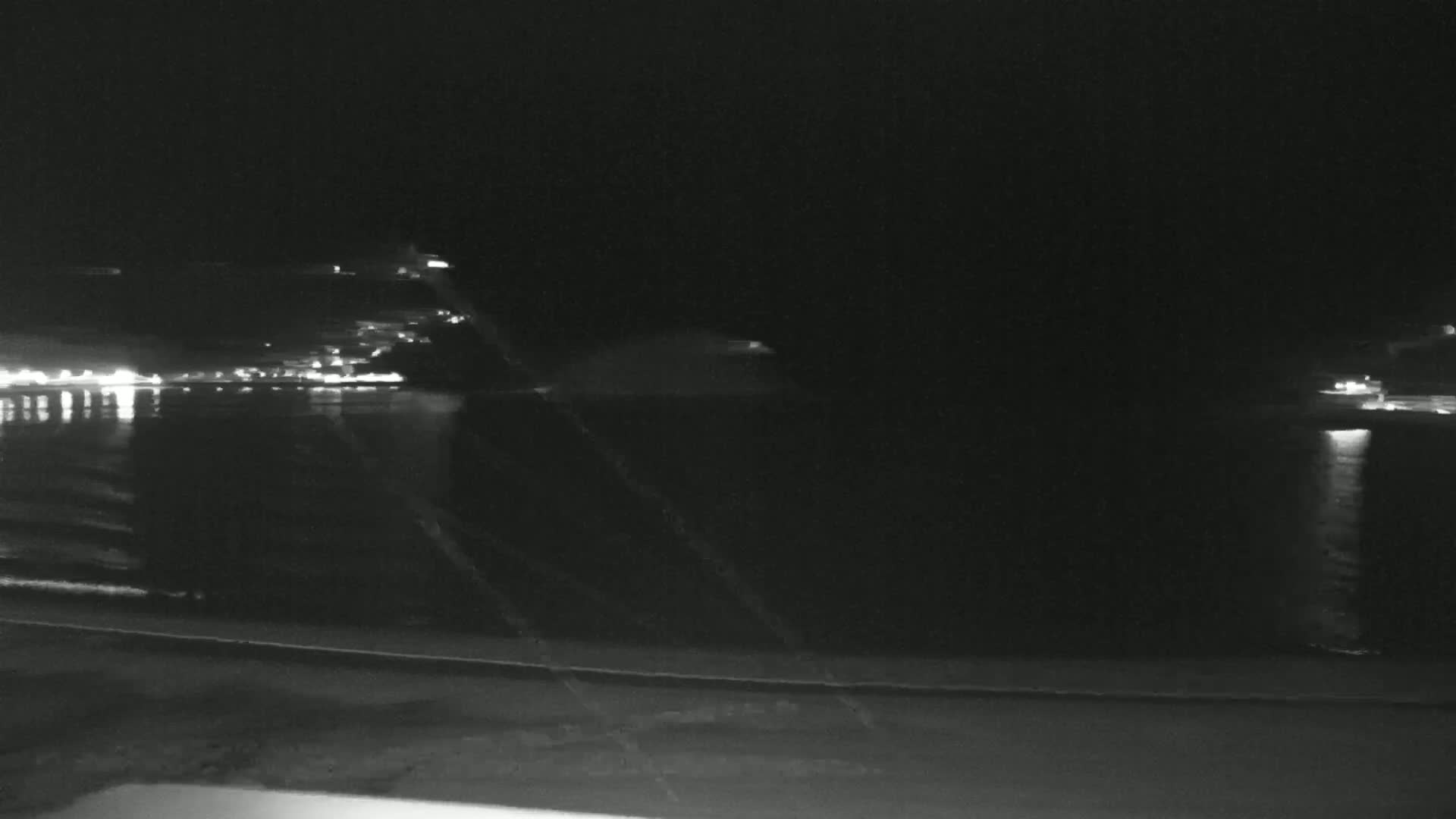 A nighttime view of a calm body of water reflecting the lights of a distant shoreline.