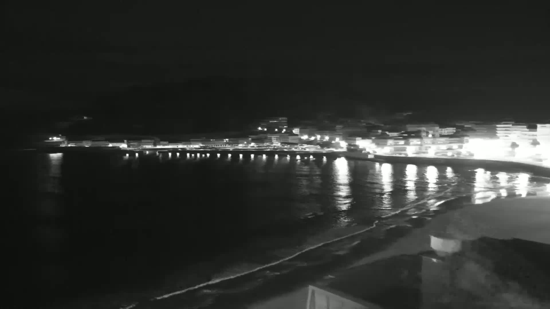 A nighttime, low-light view of a coastal town with lights reflecting on a calm sea.