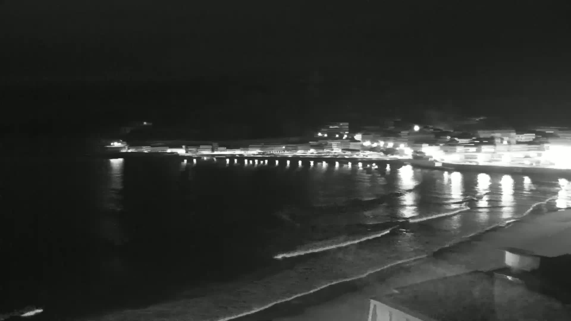 A nighttime view of a coastal town with lights reflecting on the gently lapping waves.