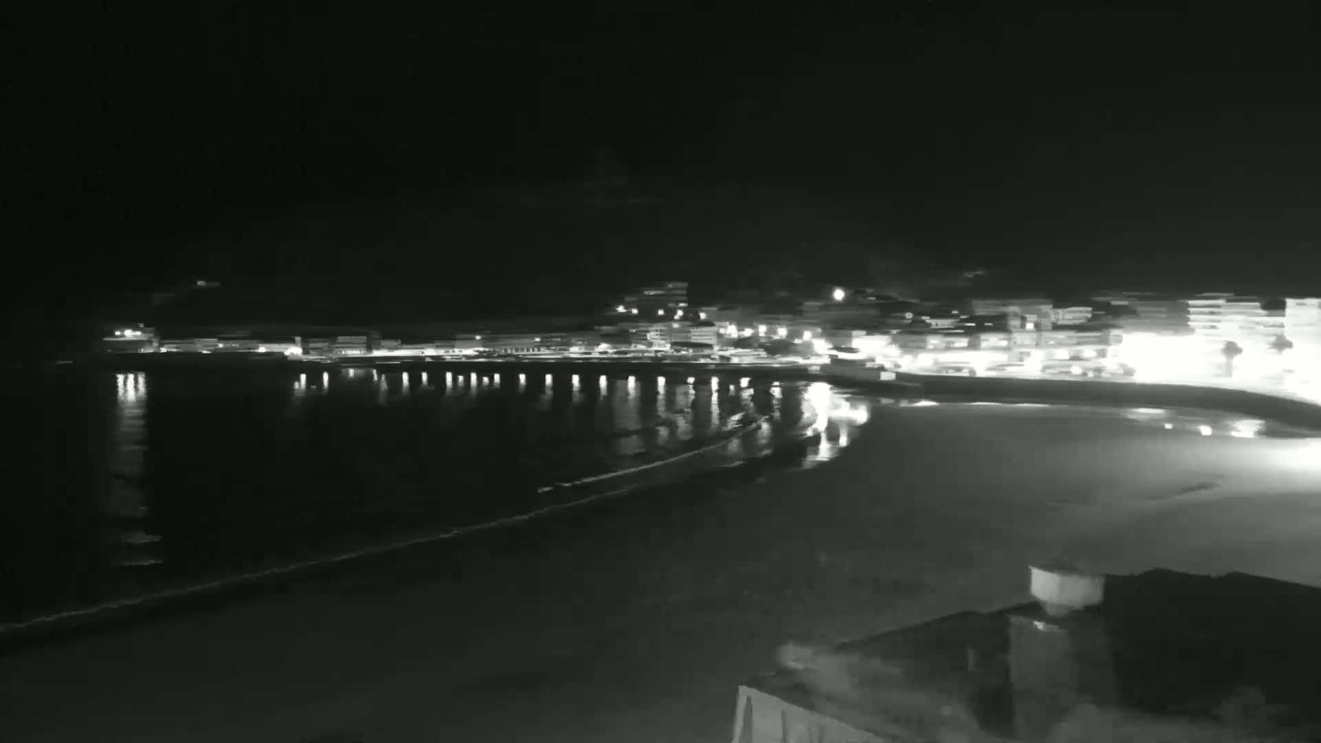 A nighttime view of a coastal town with lights reflecting on a calm, dark ocean.