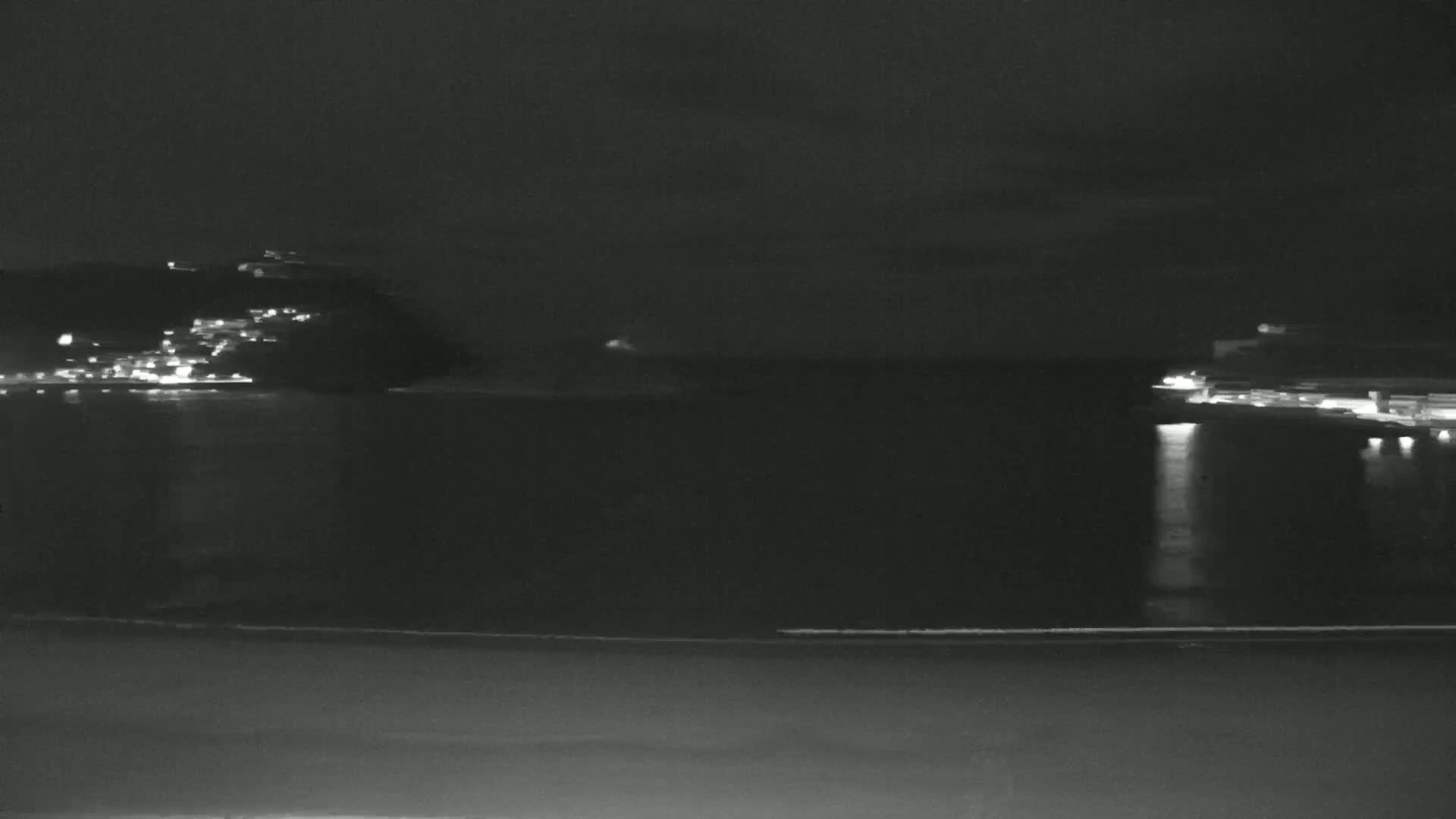 A nighttime view of a calm body of water reflecting the lights of buildings on opposite shores under a dark sky.