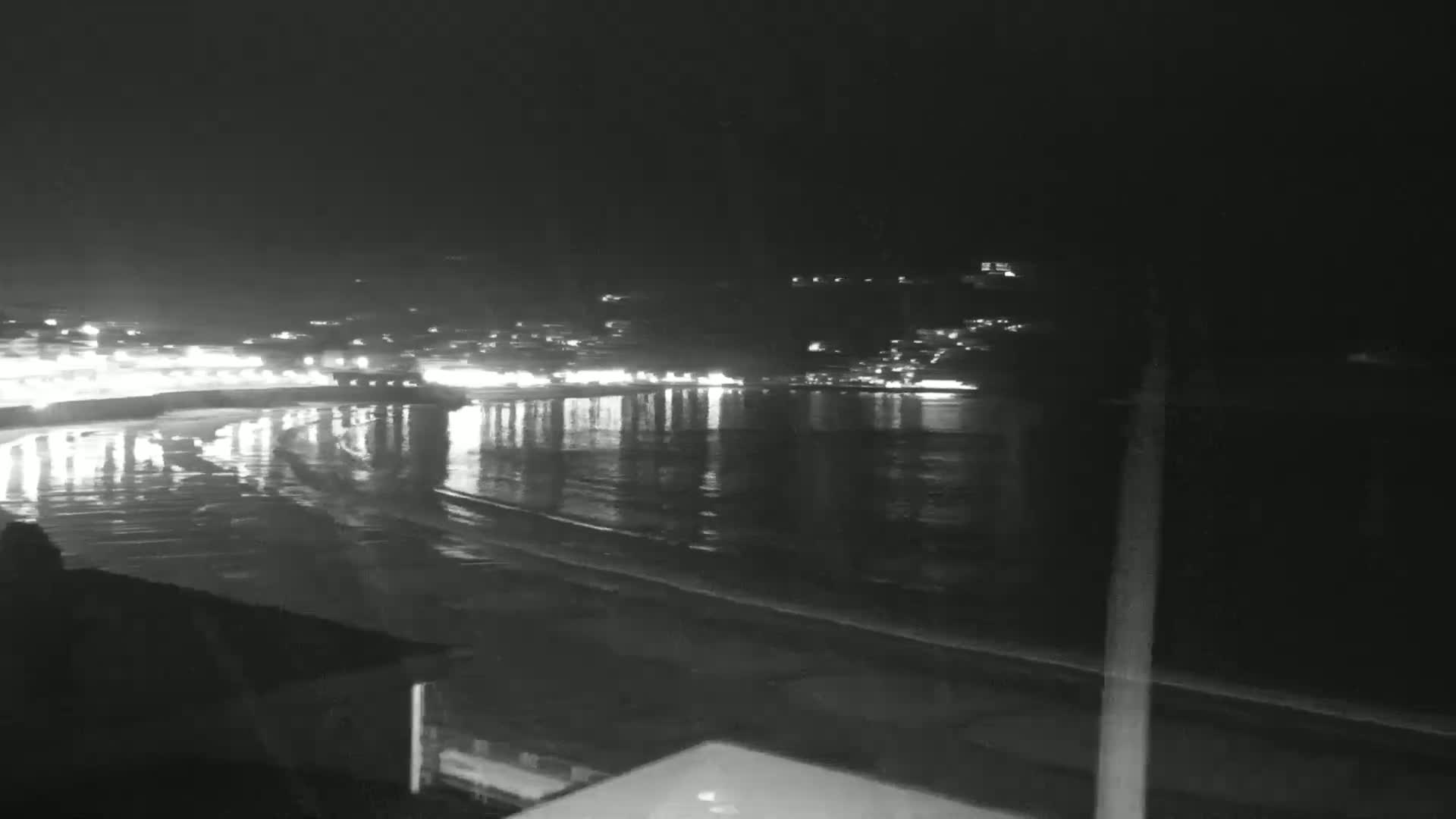 A nighttime view of a calm, dark-colored body of water reflecting the lights of a town on the opposite shore.