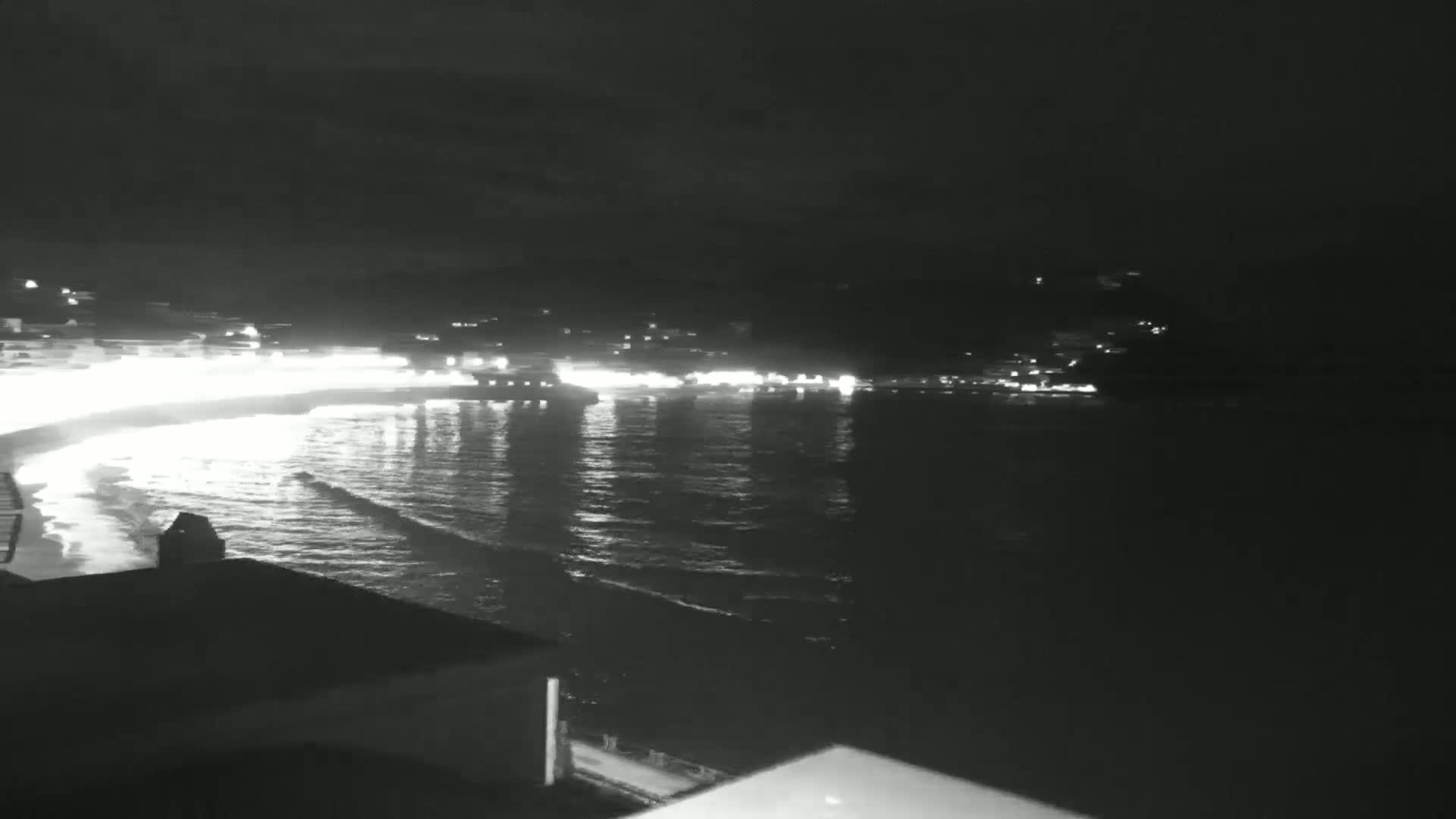 A nighttime view of a calm ocean with a dimly lit beach and town along the shore.