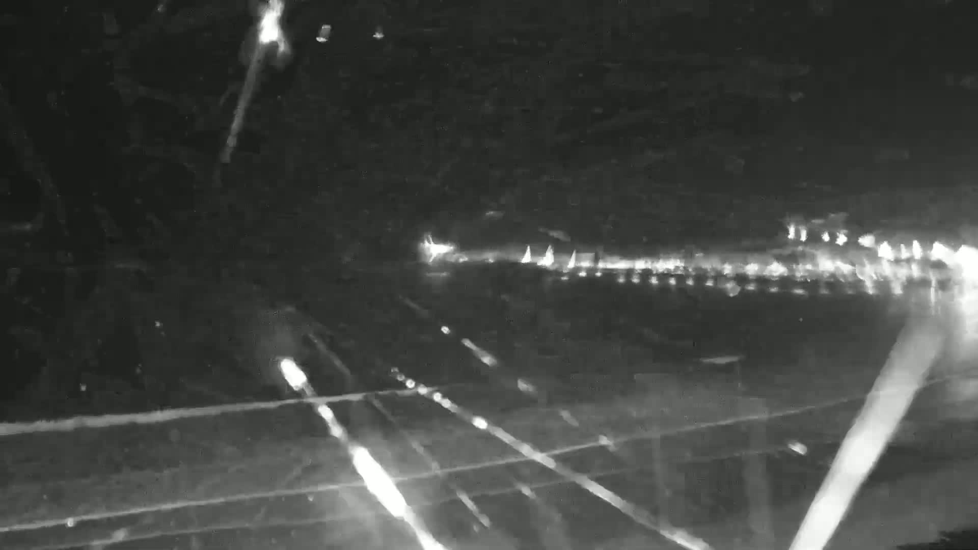 A nighttime view of a highway with bright streaks of light from moving vehicles, possibly under slightly snowy or dusty conditions.
