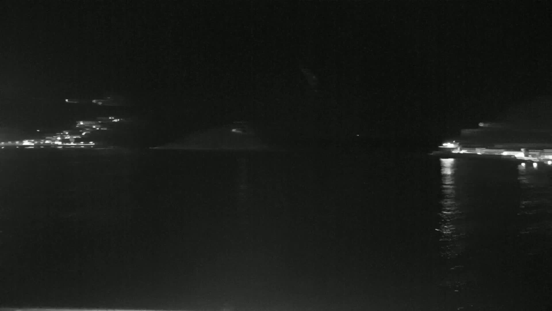 At night, faint lights illuminate a body of water with dimly lit shorelines on either side.