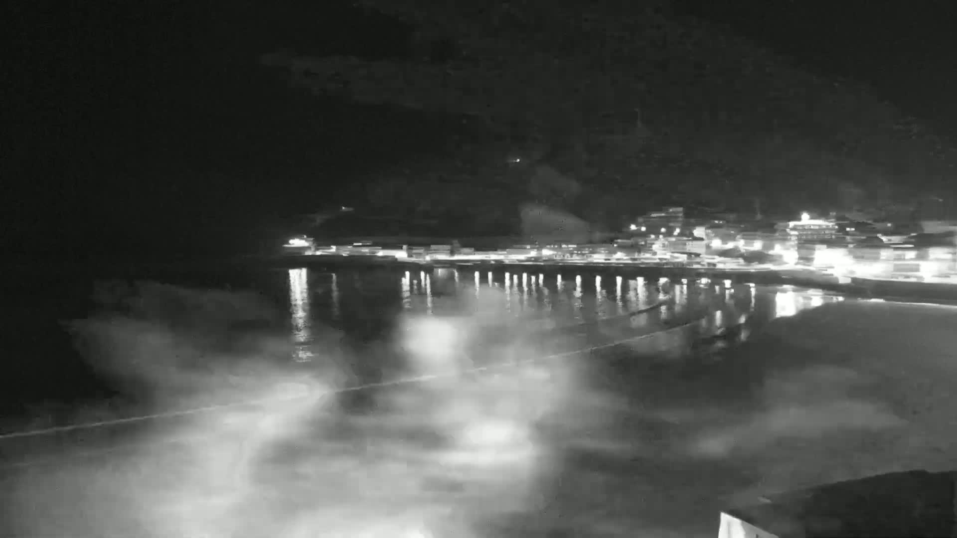 A nighttime, low-light view of a town's waterfront at night, with lights reflected on the calm water.