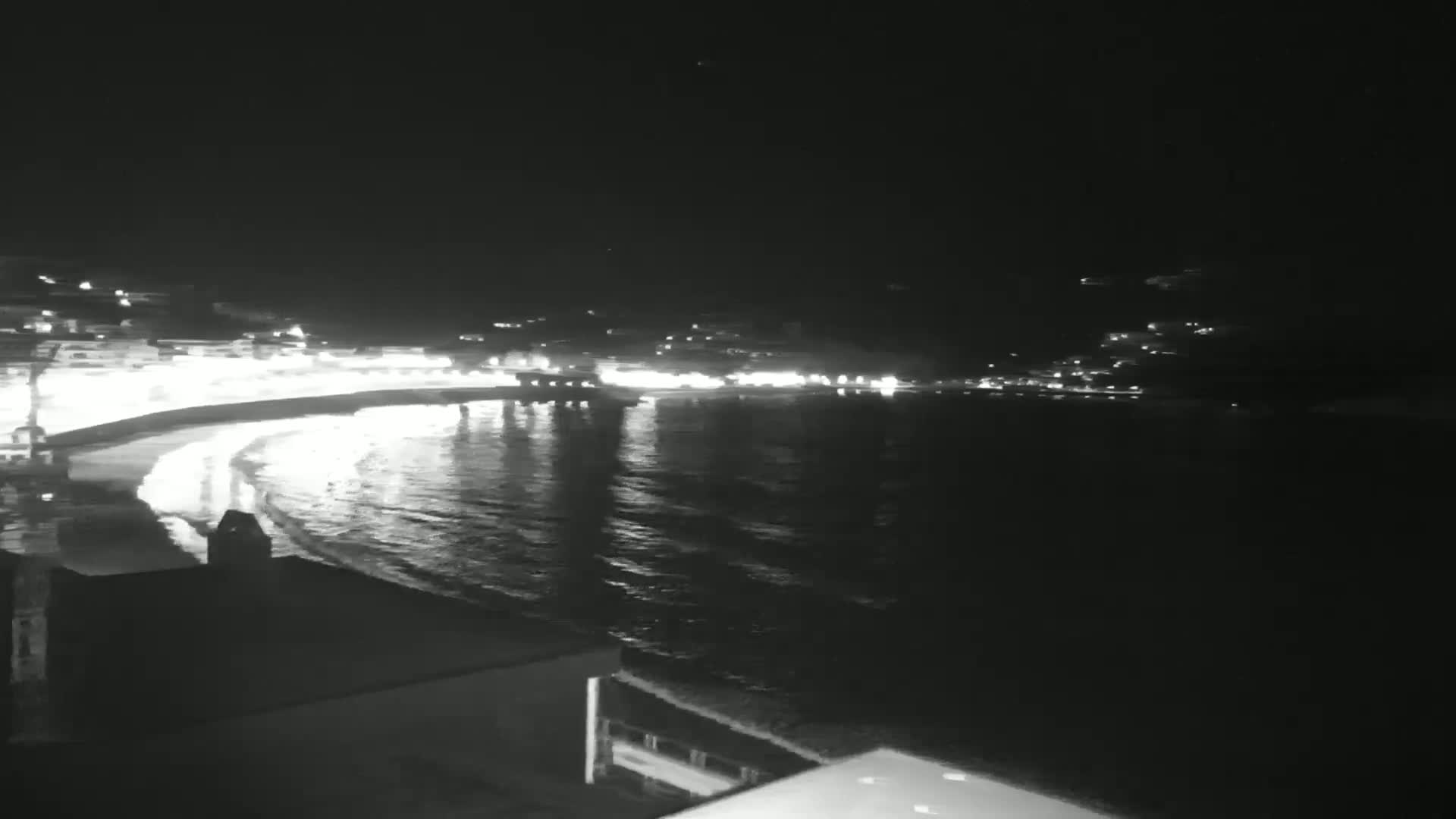 A nighttime view of a calm ocean reflecting the lights of a town on a shoreline.