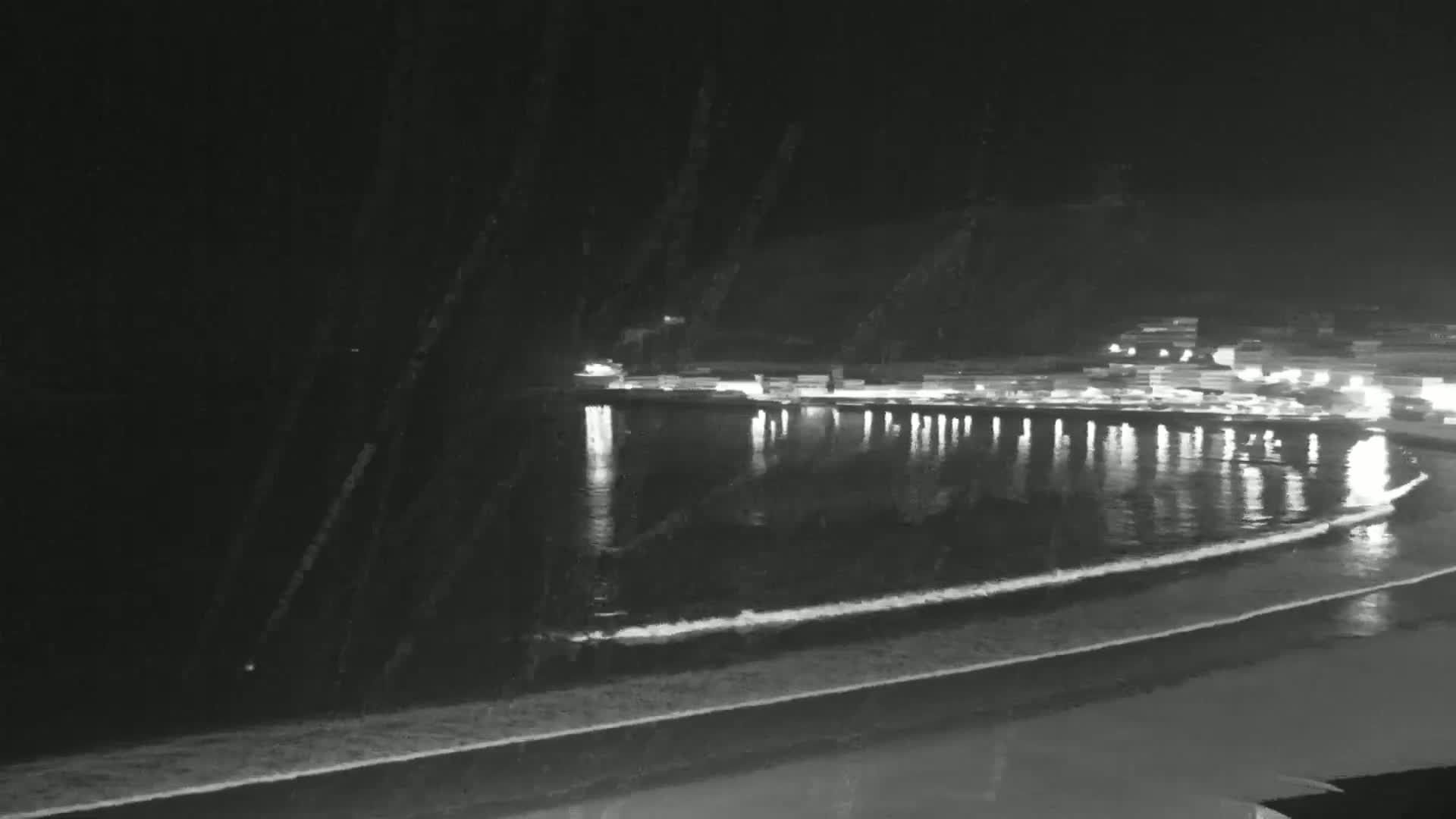 A nighttime view of a calm ocean bay with a shoreline of lights reflecting on the water's surface.