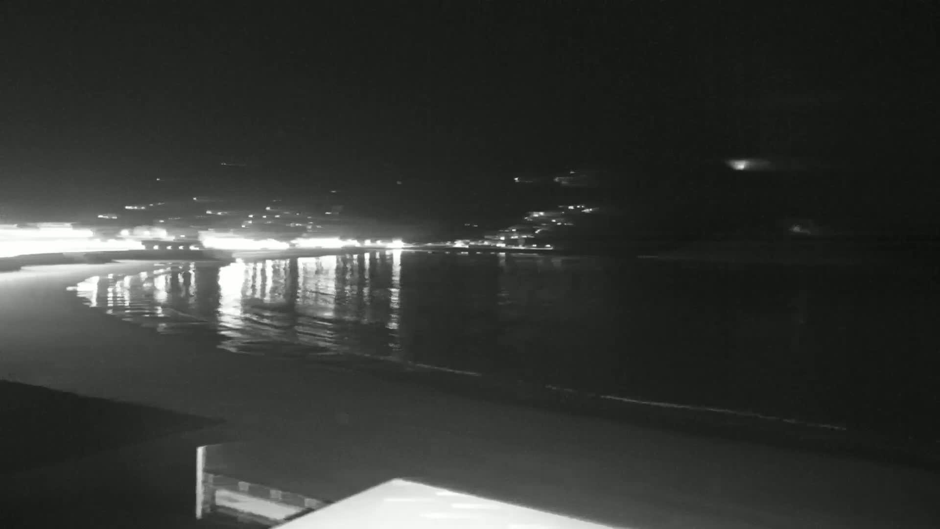 A nighttime view of a calm body of water reflecting the lights of a town on the opposite shore.