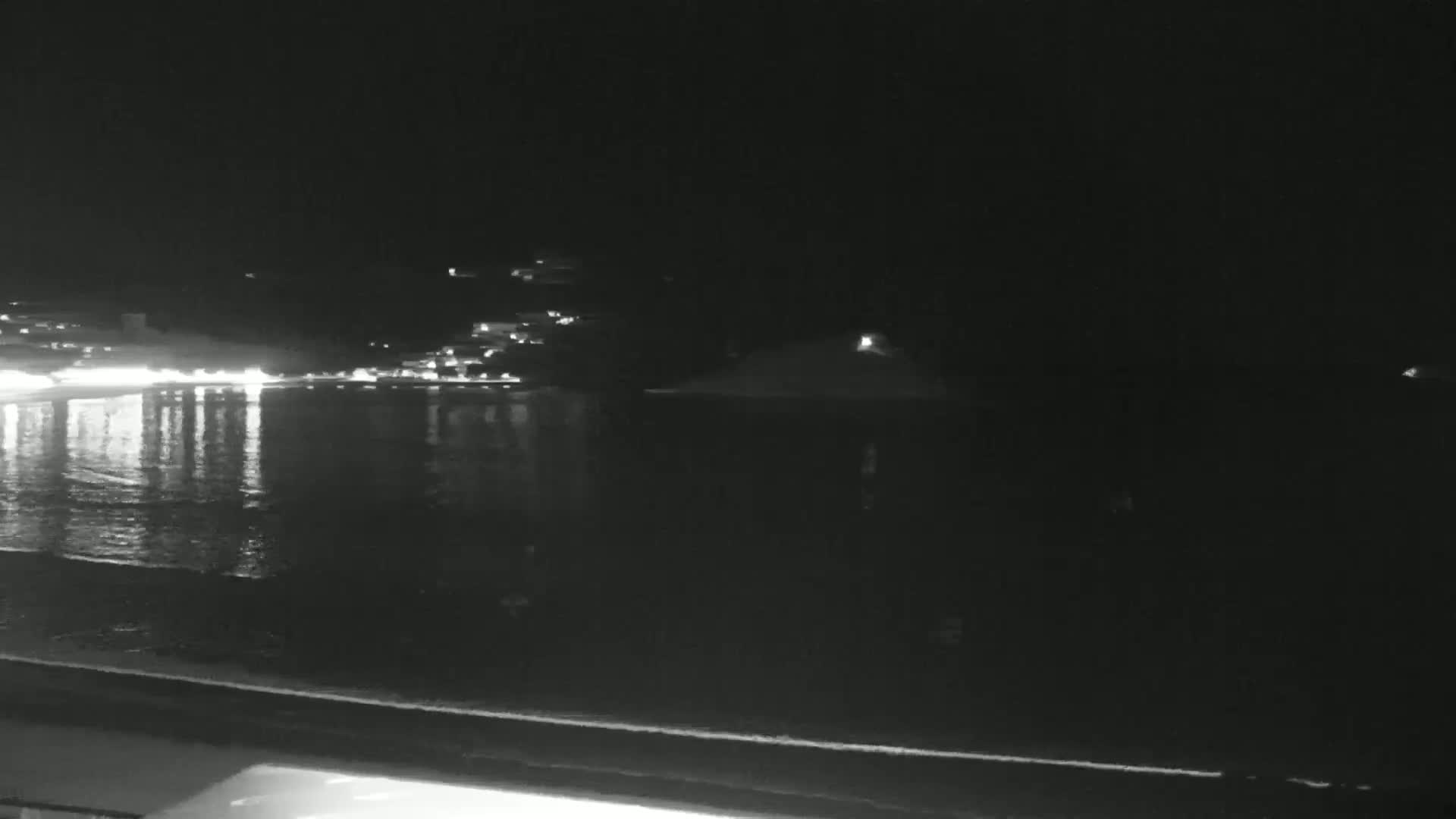 A nighttime view of a calm body of water reflecting the lights of a town on the opposite shore.