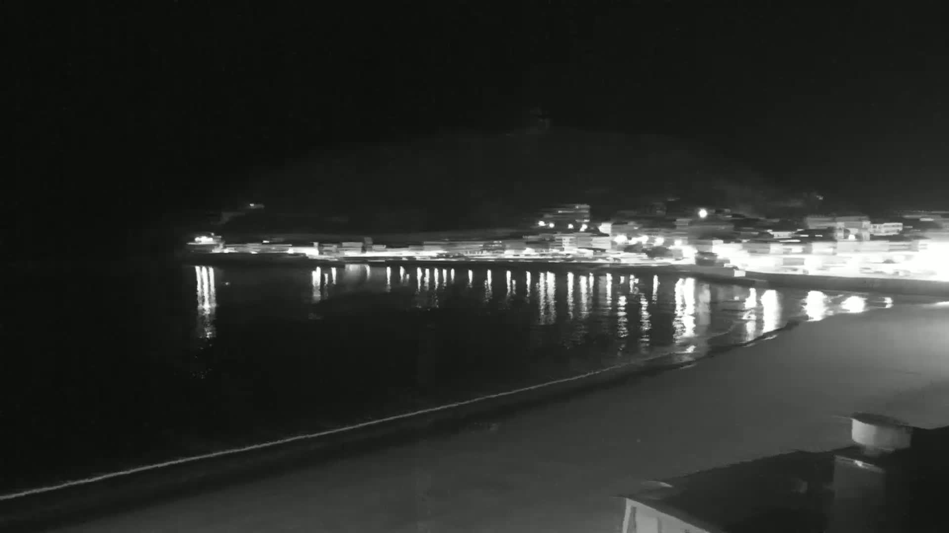 A nighttime view of a calm ocean reflecting the lights of a town on a dark shore.
