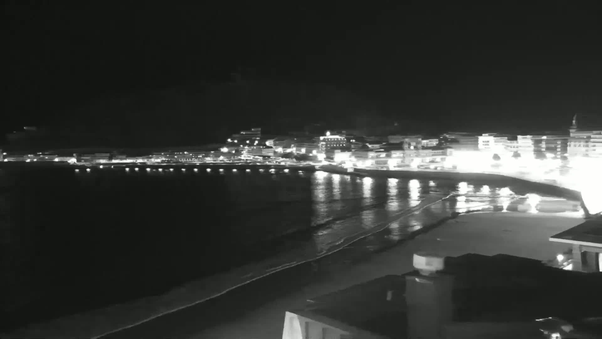 A nighttime view of a brightly lit coastal town with a dark, gently lapping ocean.