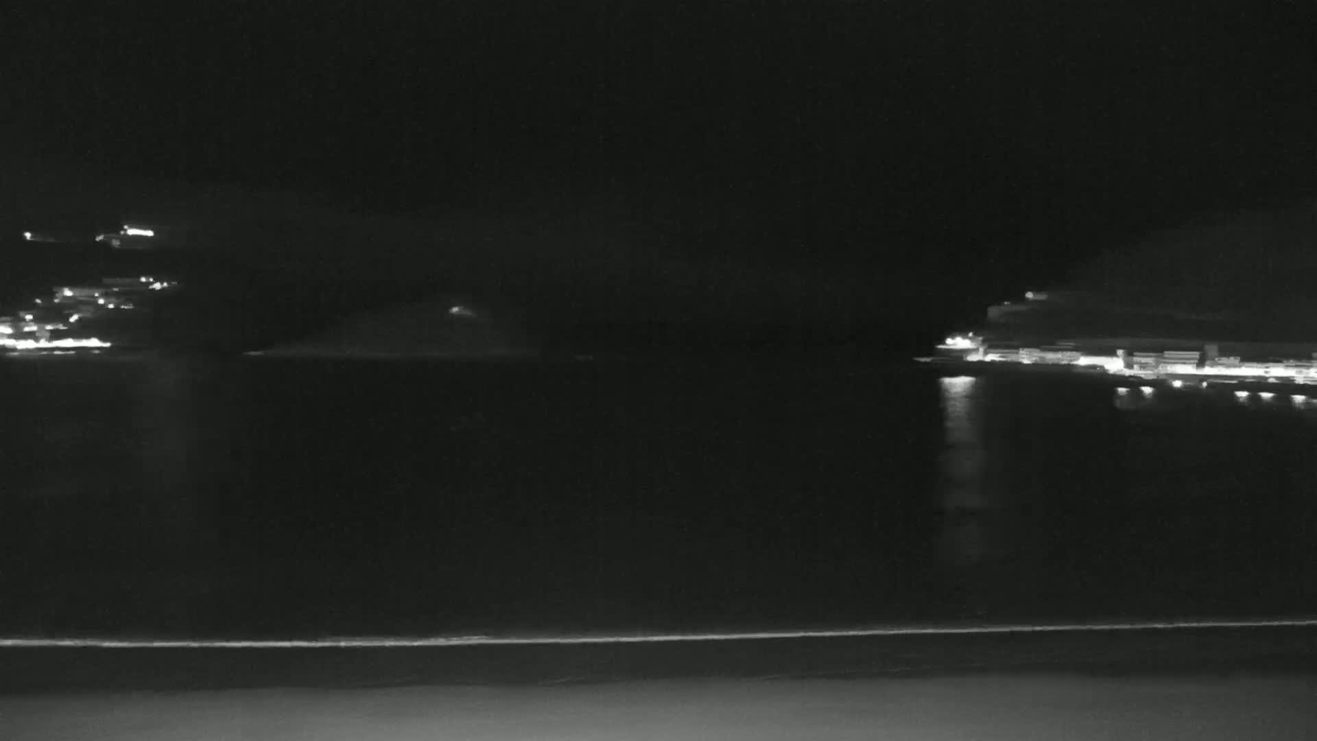 A nighttime view of a dark body of water with faintly lit shorelines and a small island in the distance.