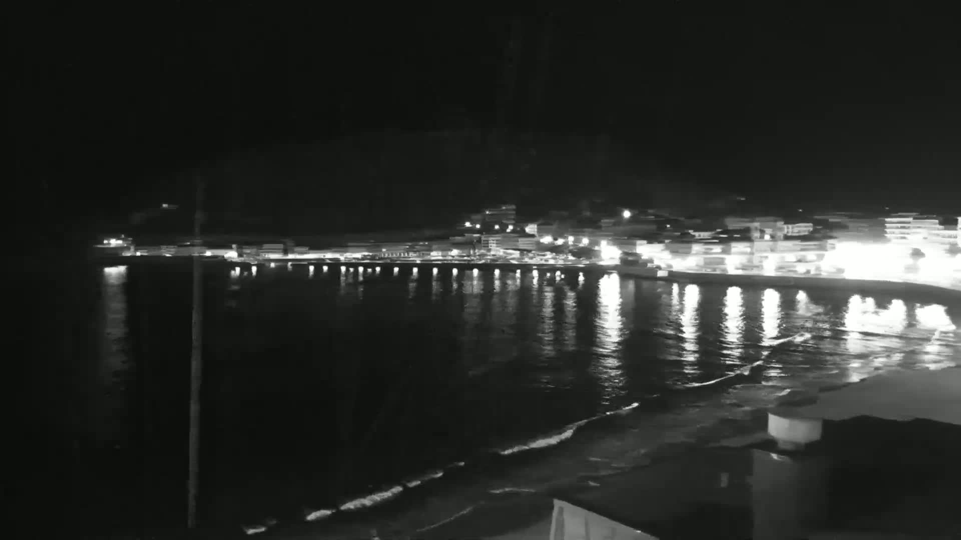 A nighttime view of a city's waterfront illuminated by lights reflecting on gently lapping waves.