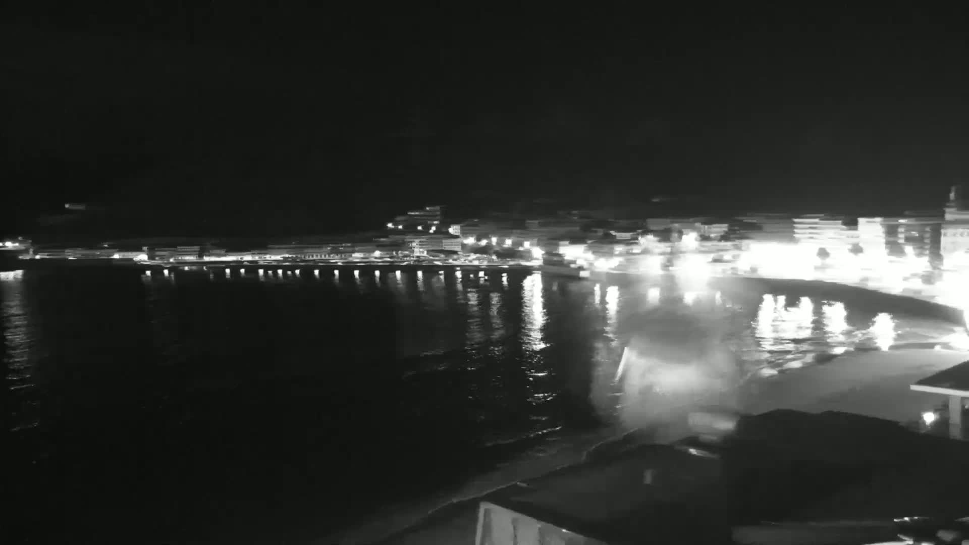 A nighttime view of a calm, dark body of water reflecting the lights of a town along its shore.