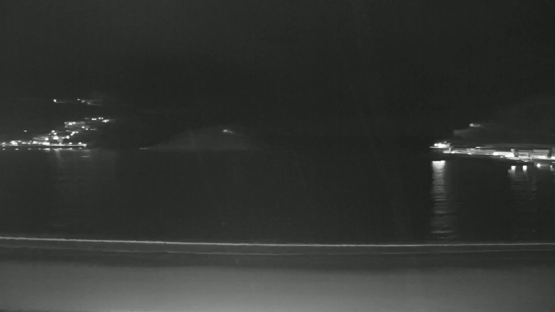 A nighttime view of a calm body of water with dimly lit shorelines and a small island in the distance.