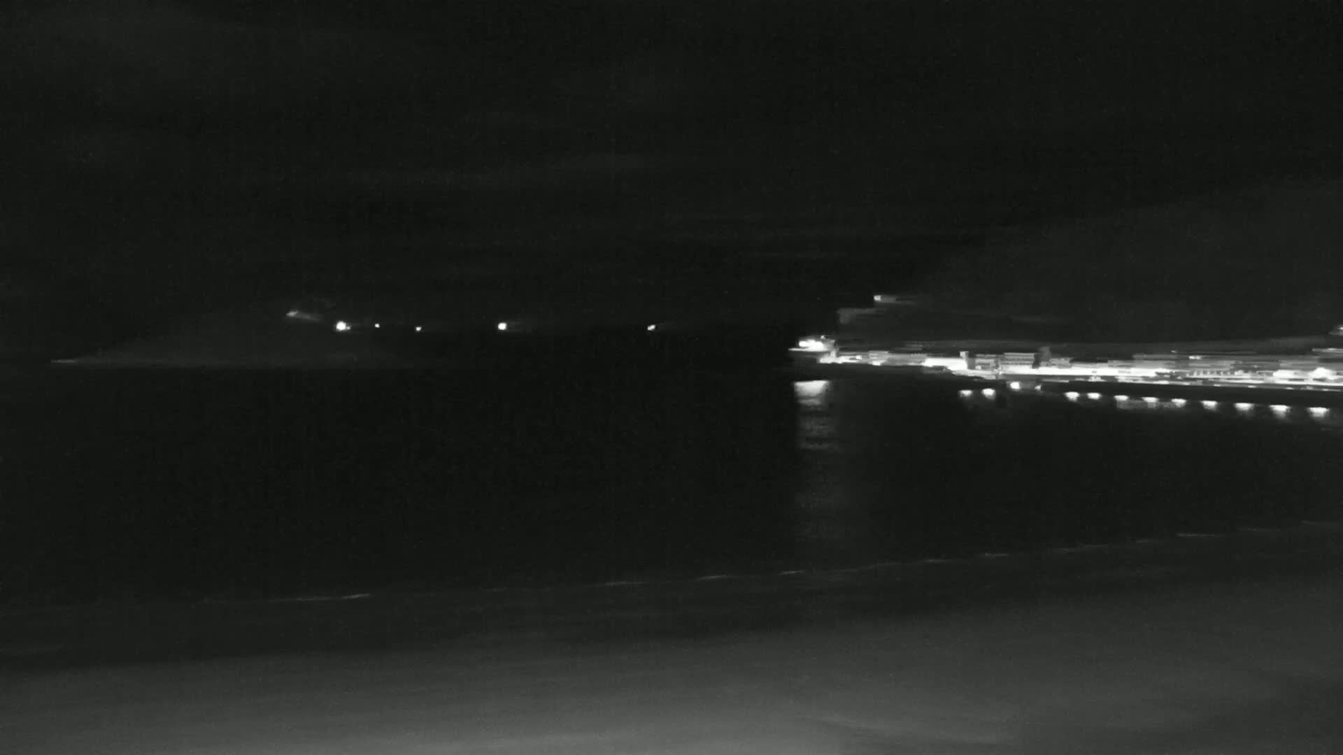 A nighttime view of a dark, calm body of water with dimly lit structures on opposite shores.