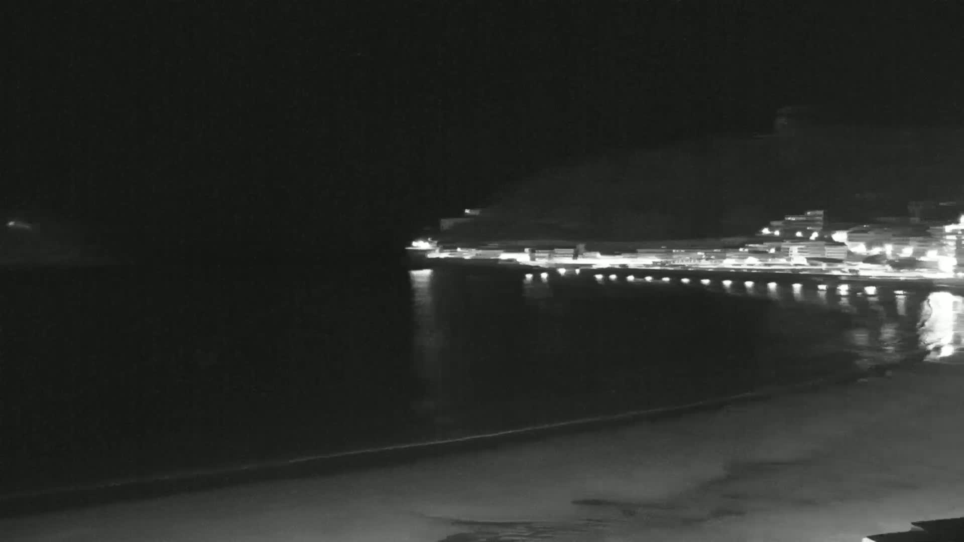 A nighttime view of a calm ocean reflecting the lights of a town built on a hillside.