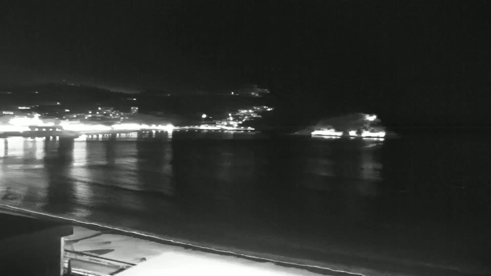 A nighttime view of a calm body of water reflecting the lights of a town on the opposite shore.