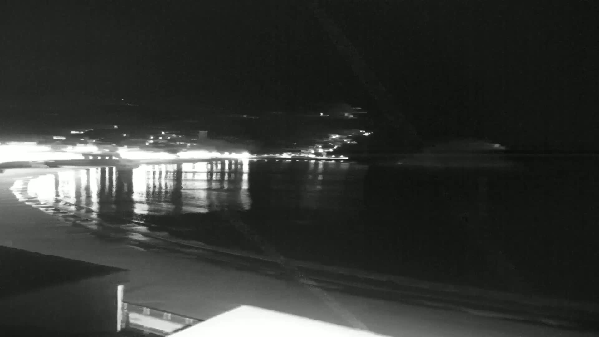 Lights from a town across a dark, calm body of water reflect on the surface at night.