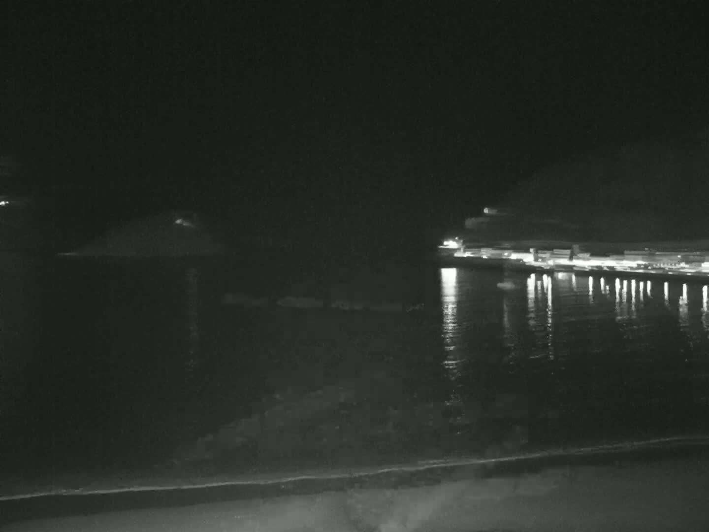 A nighttime view of a calm body of water reflecting the lights of a distant shoreline.