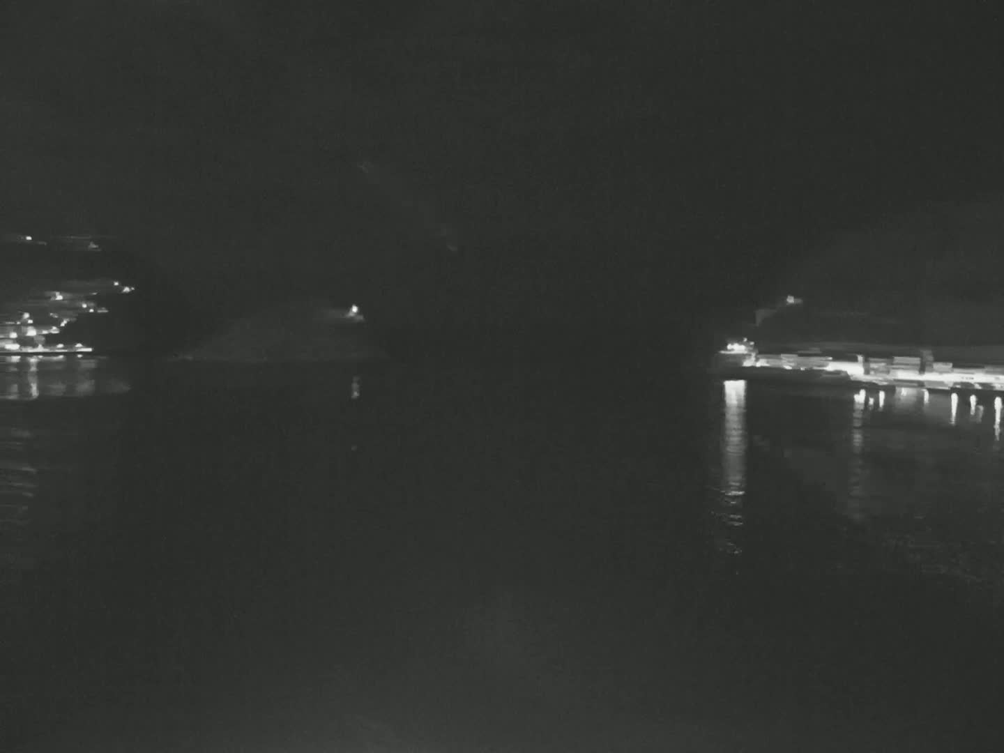 At night, a dark body of water reflects the lights from buildings and structures on either shore.