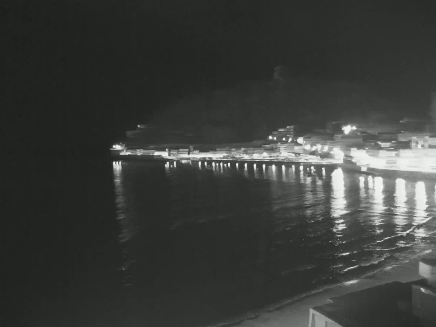 A nighttime view shows a calm body of water reflecting the lights of a town along its shore.