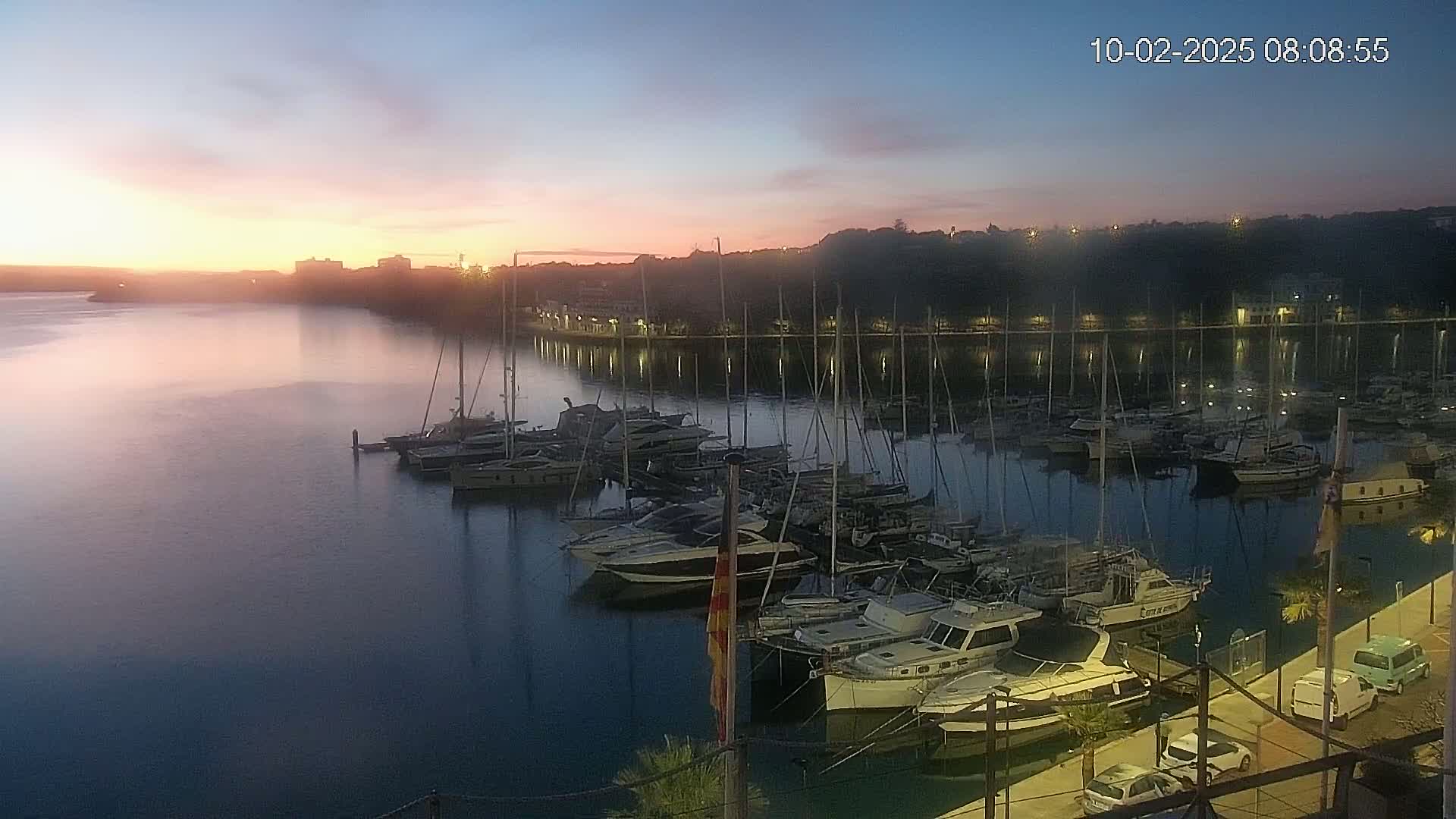 Many boats are docked in a marina at sunrise, with a calm body of water reflecting the pink and orange sky.