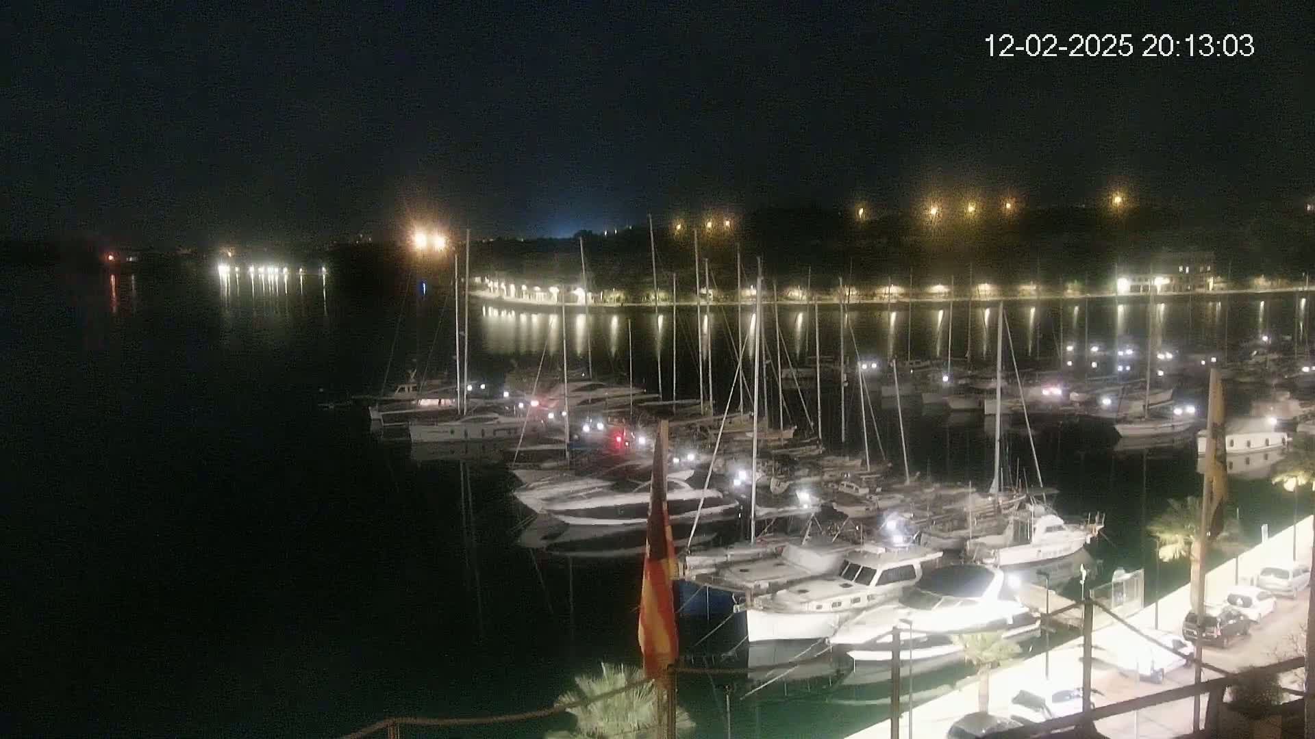 A nighttime view of a marina filled with docked boats, illuminated by lights along the waterfront and on the boats themselves.