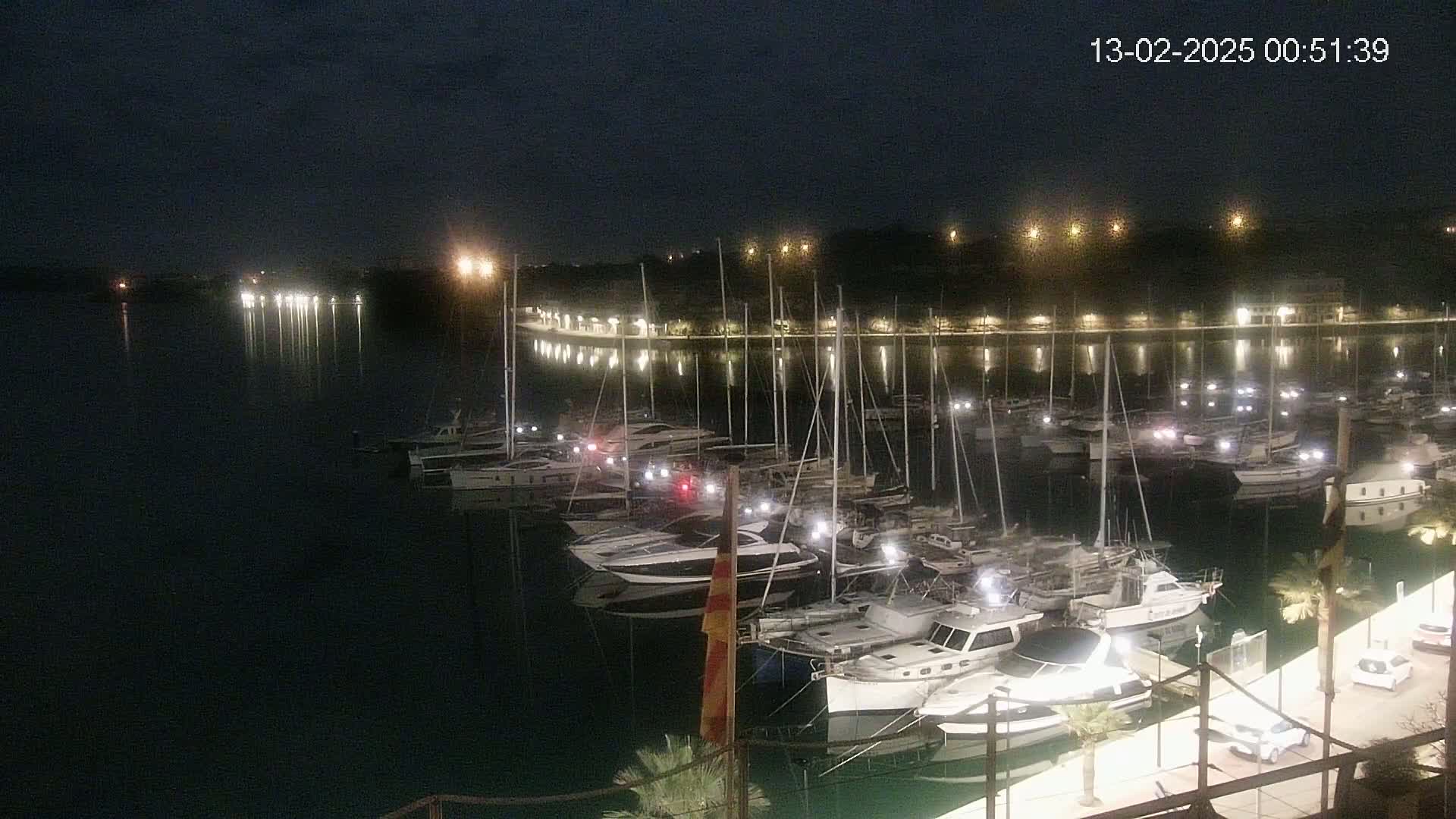 Many boats are docked at a marina at night under a dark sky.