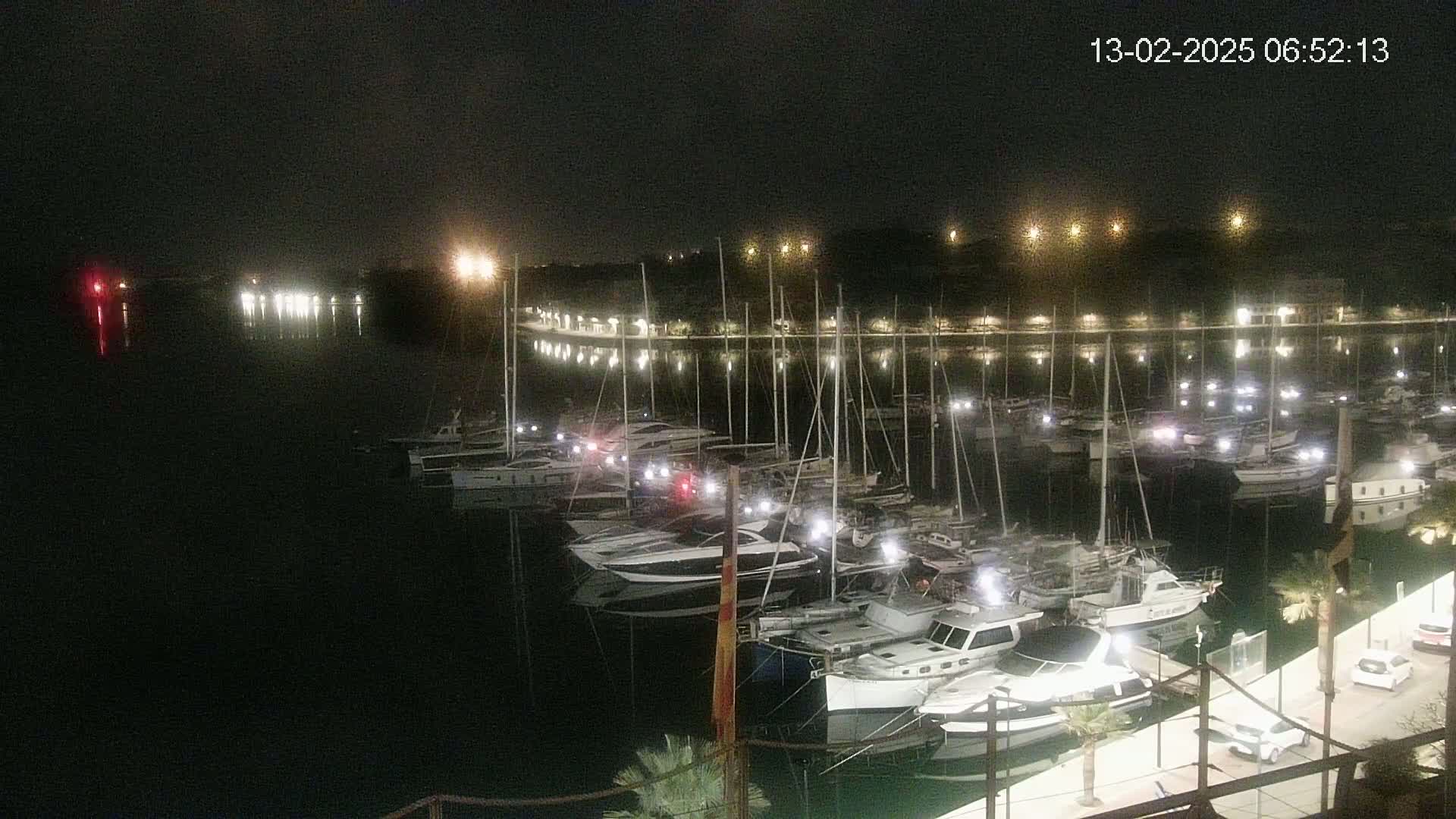 Many boats are docked at a marina at night under a dark sky.