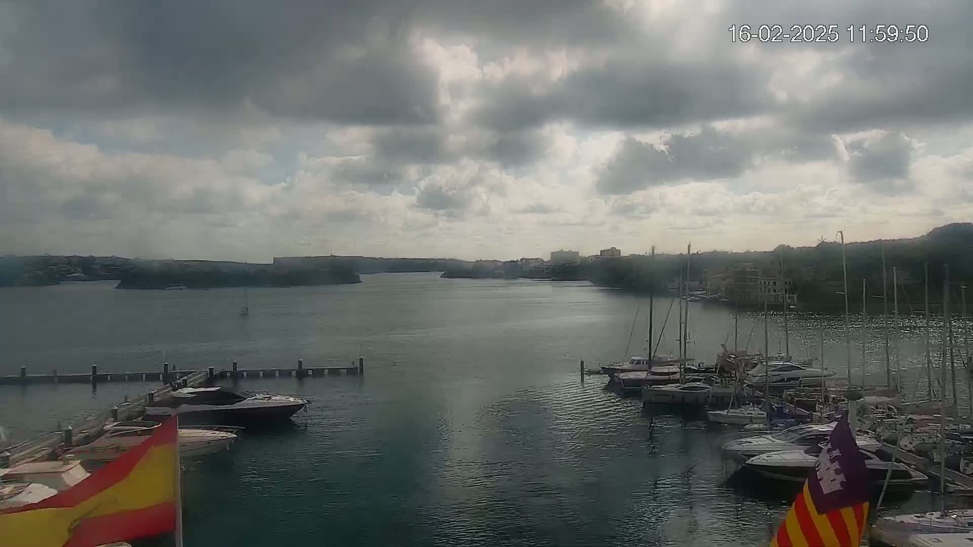 A harbor filled with moored boats is seen under a mostly cloudy sky.