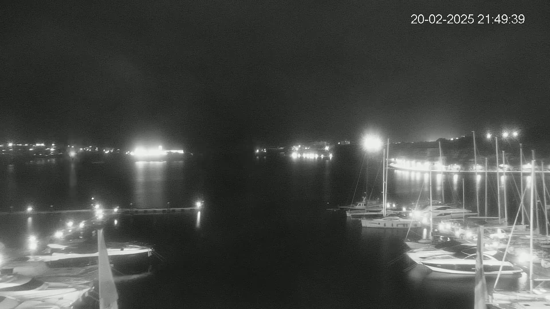 A nighttime view of a harbor filled with moored boats, illuminated by lights on the shore and across the water.
