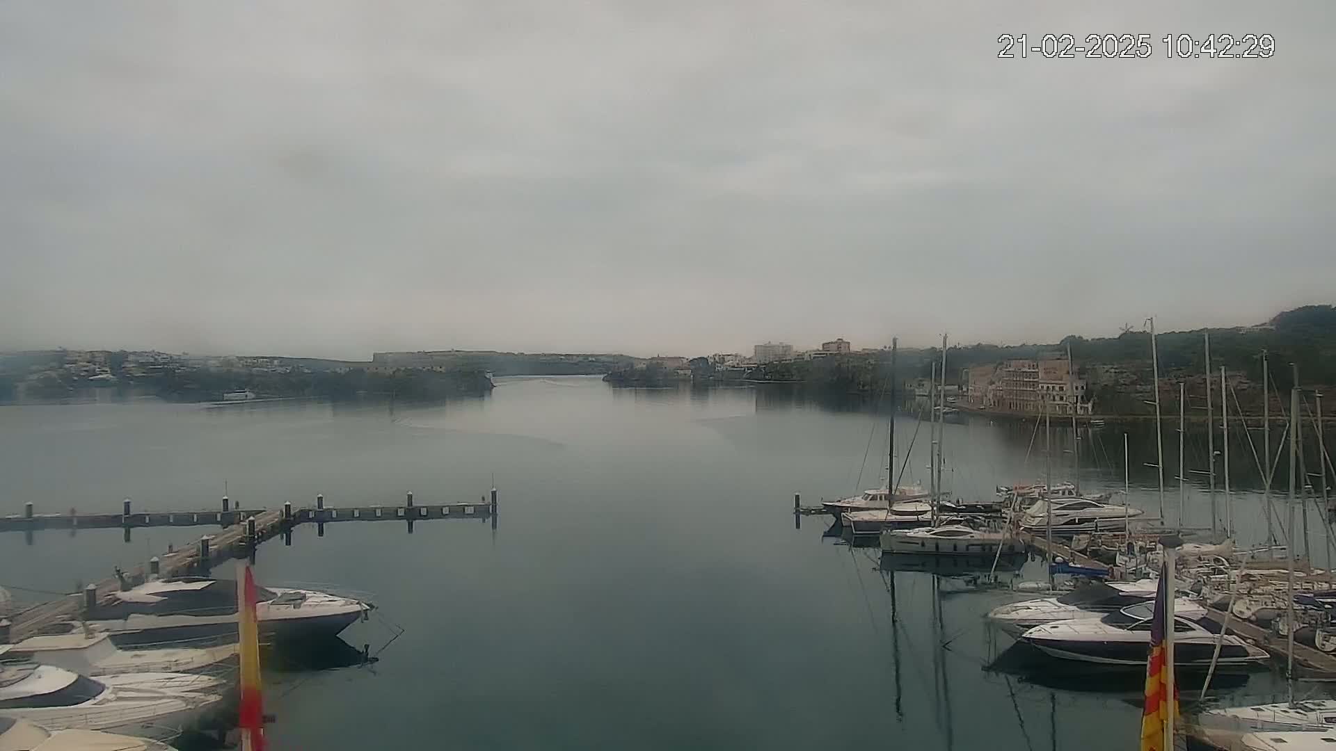 A calm harbor filled with numerous yachts and sailboats is seen under an overcast sky.