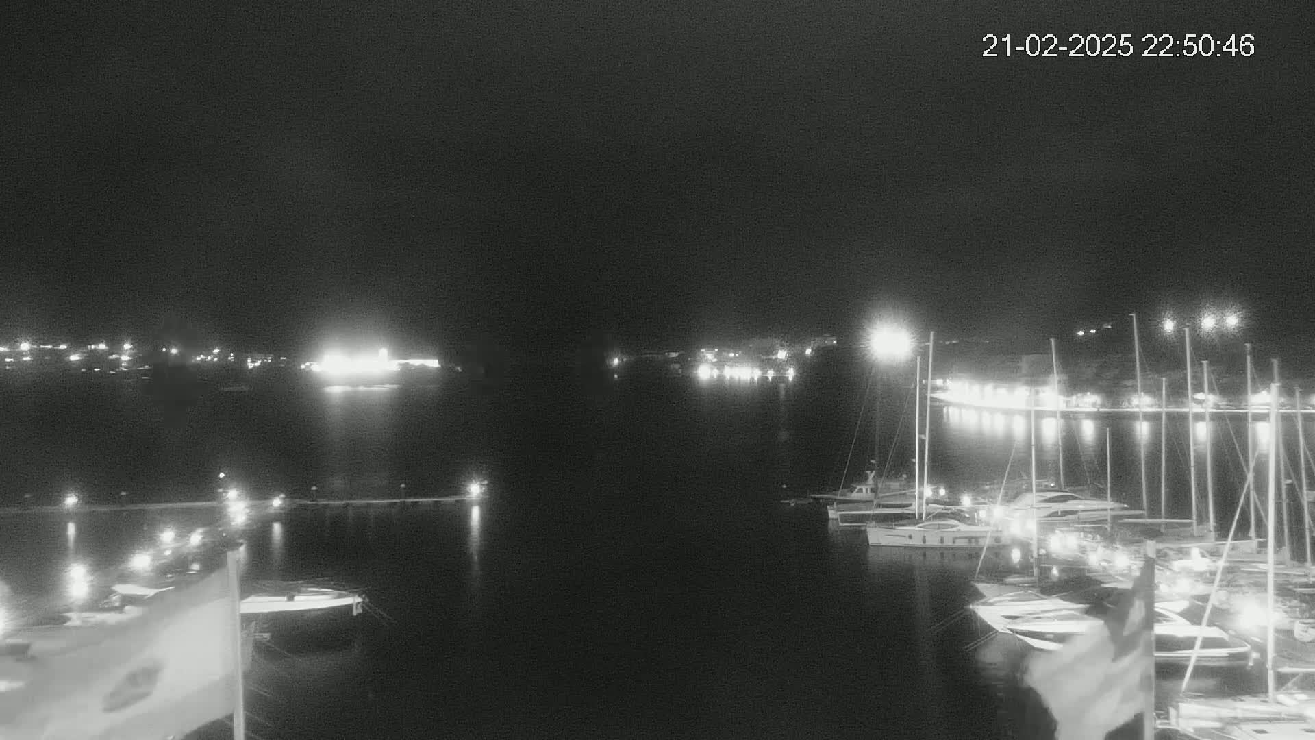 A nighttime view of a harbor filled with boats, illuminated by lights from the docks and surrounding buildings under a clear, dark sky.