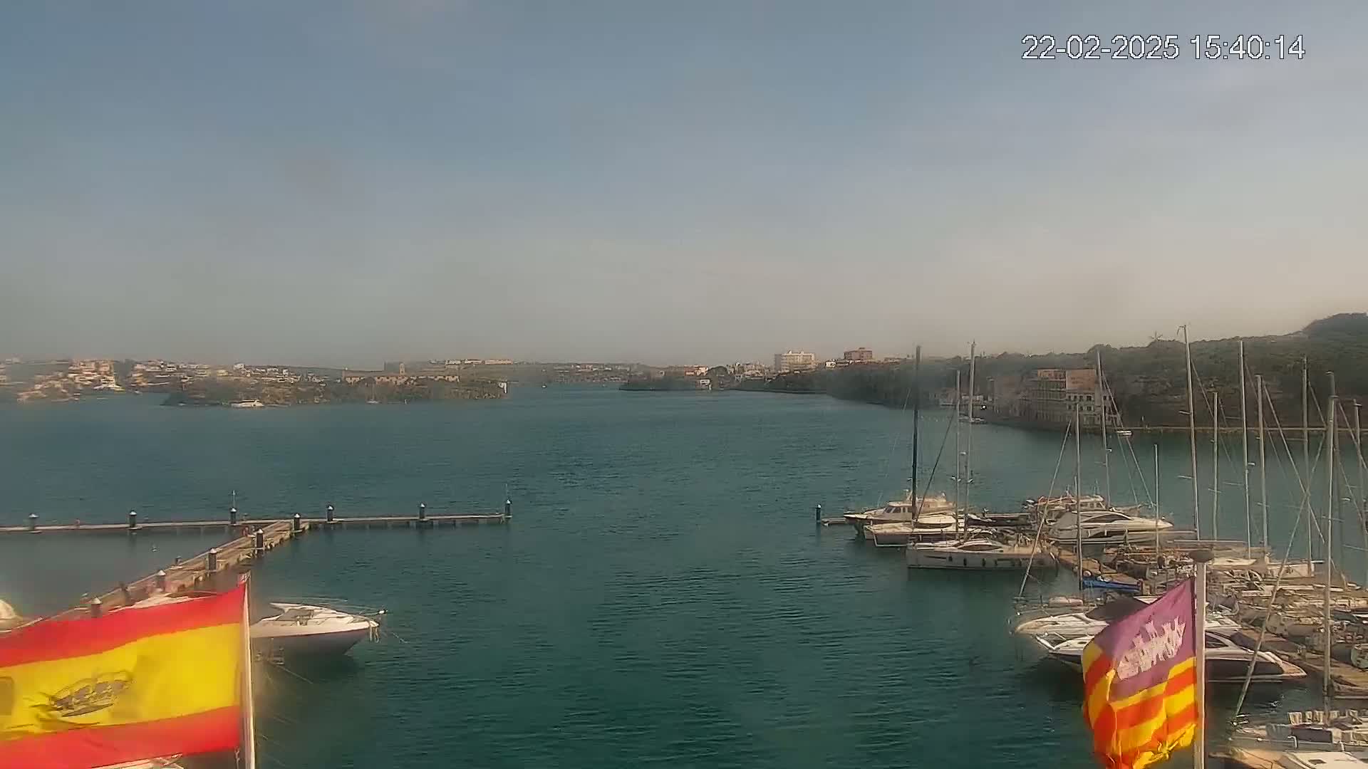 A marina filled with sailboats and motorboats is situated in a calm bay under a clear, hazy sky.
