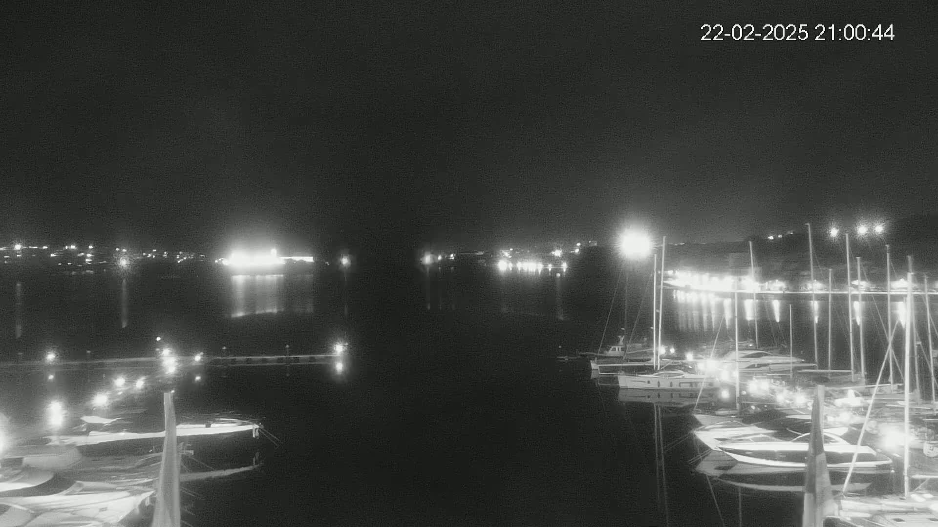 A nighttime view of a harbor filled with docked boats and illuminated by lights from the shore and vessels, under a clear, dark sky.