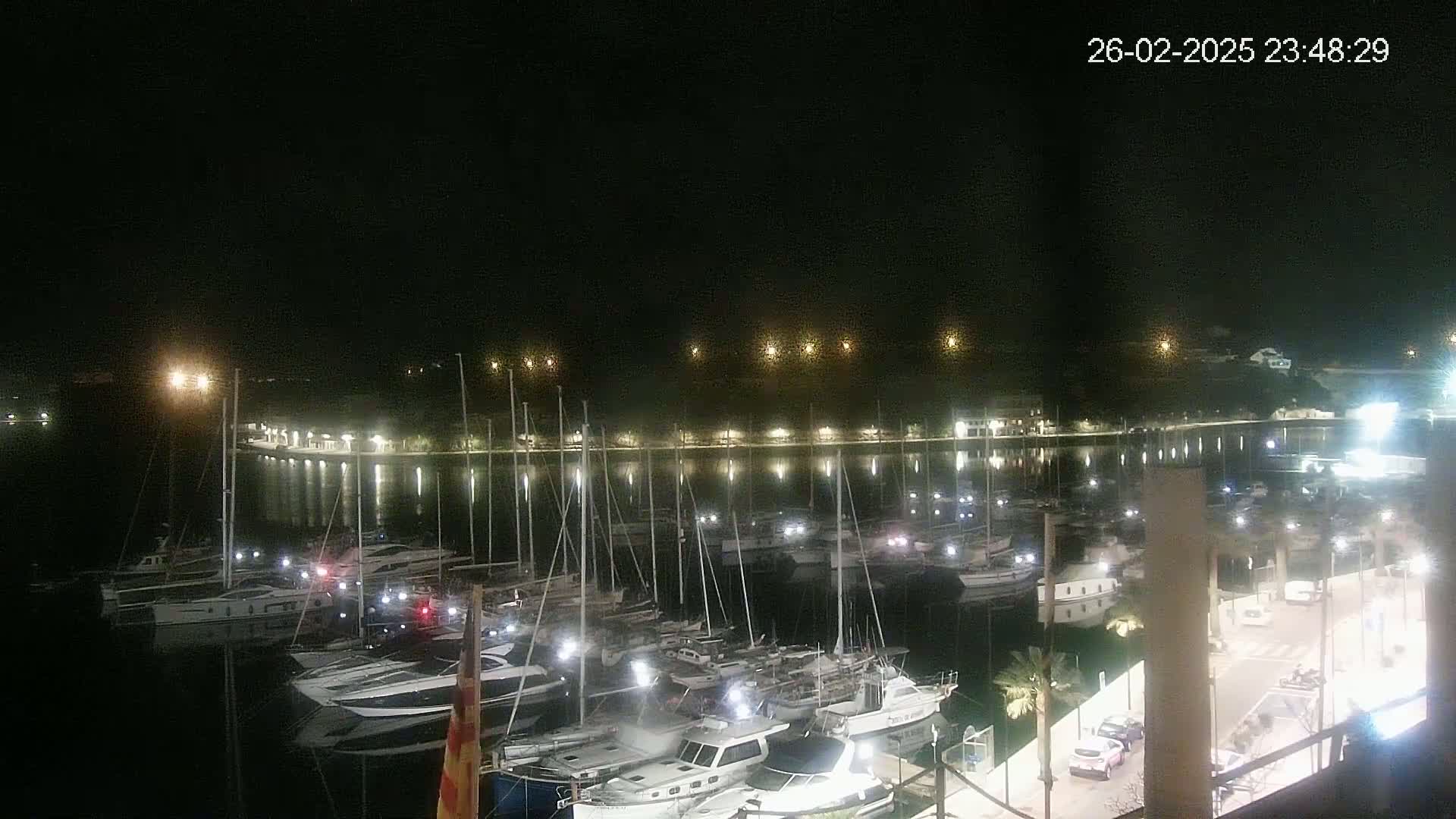 A nighttime view of a marina filled with many boats, illuminated by lights along the docks and buildings on the shore.