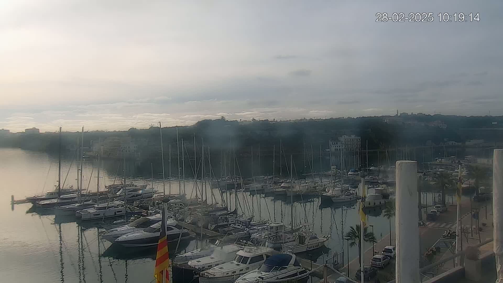 A marina filled with numerous sailboats and motorboats is seen on a calm, overcast day.