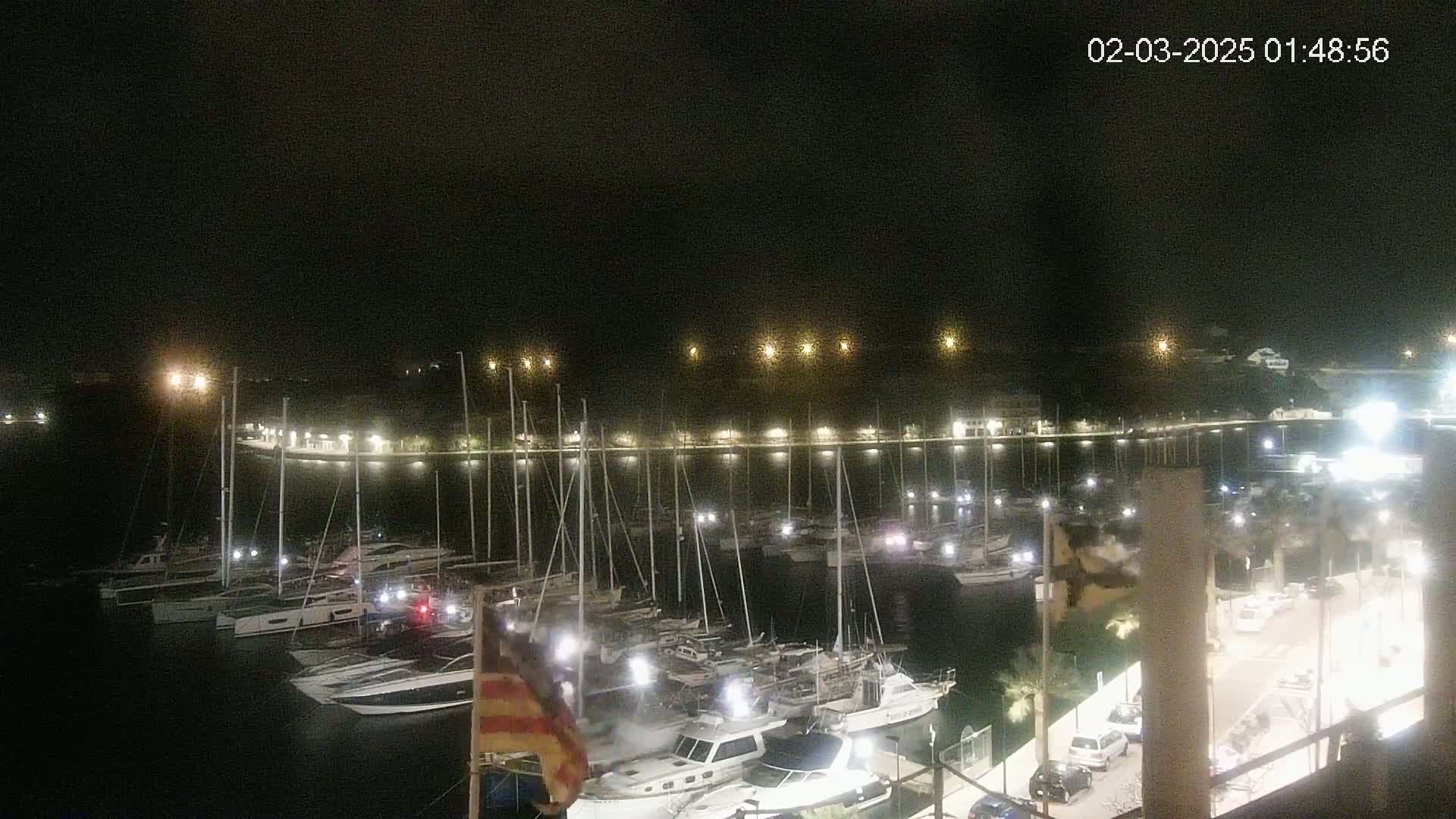 A nighttime view of a harbor filled with docked sailboats and motorboats under a clear, dark sky.