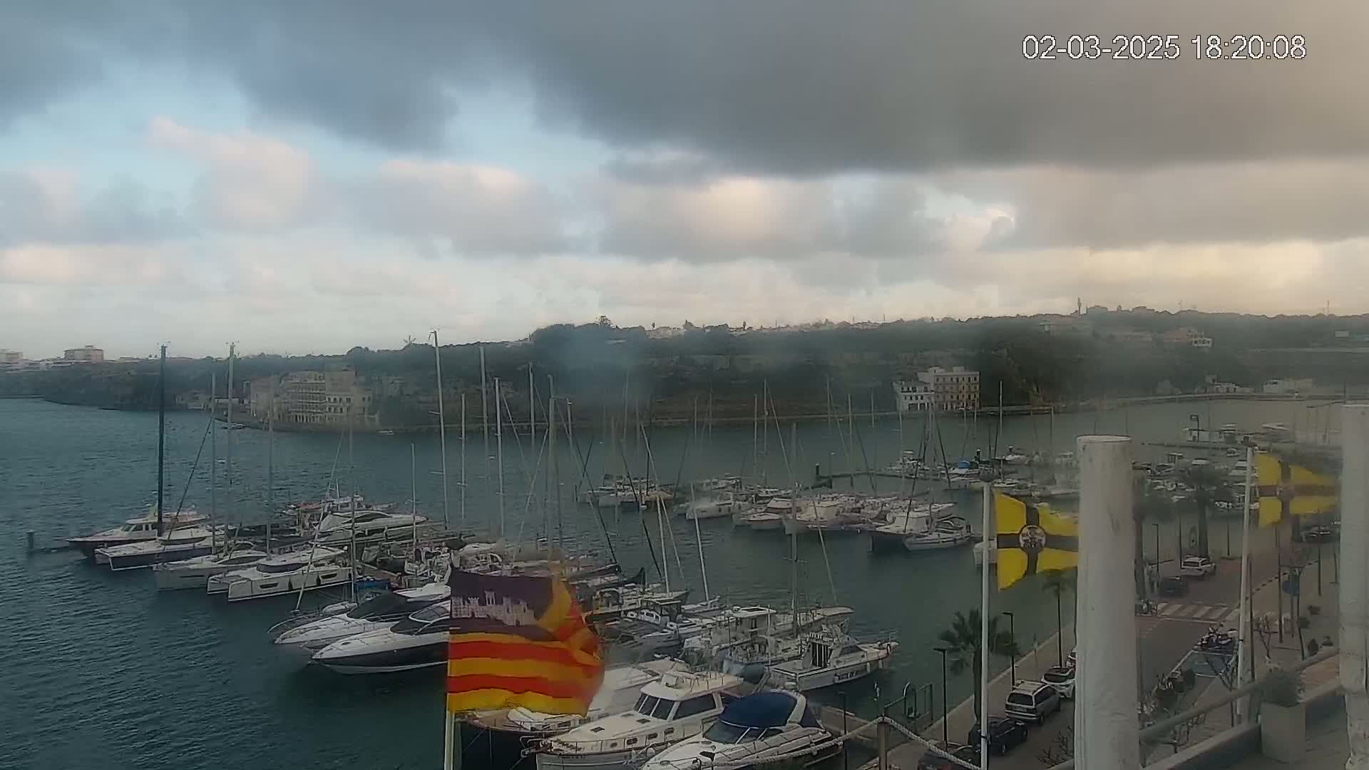 A marina filled with numerous sailboats and motorboats is shown under a cloudy sky.