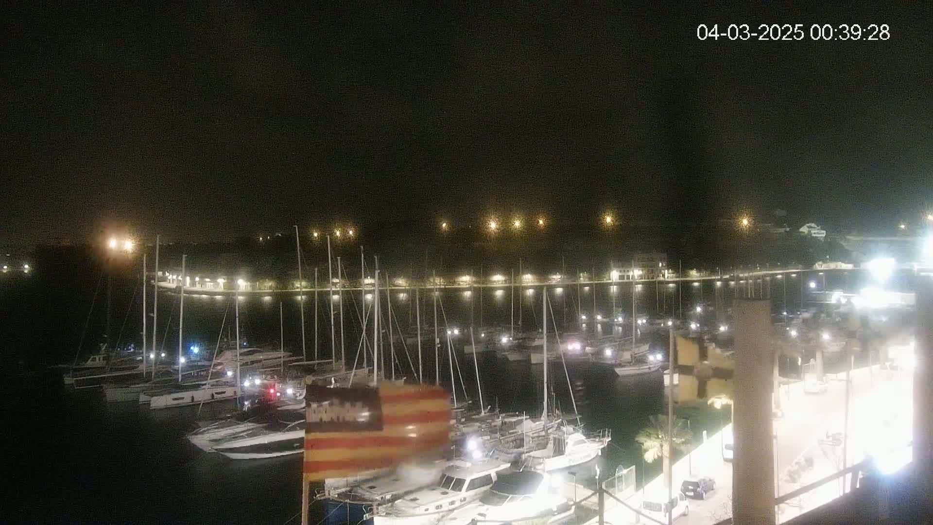A nighttime view of a marina filled with boats, illuminated by lights along the waterfront under a clear, dark sky.