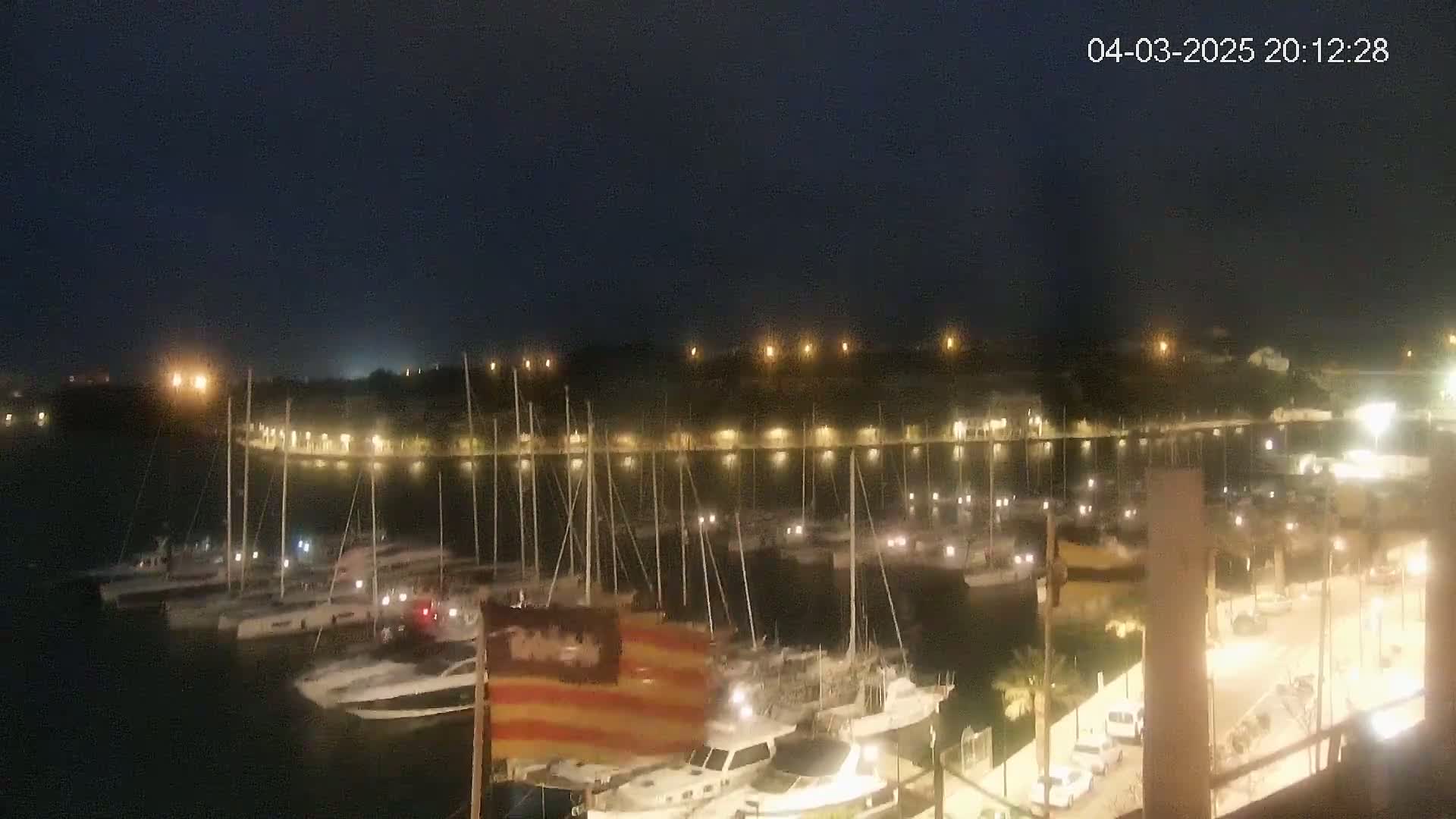 A nighttime view of a harbor filled with boats, illuminated by lights along a shoreline.